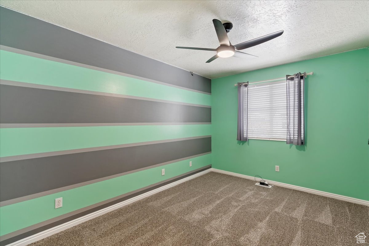 Unfurnished room featuring ceiling fan, carpet, and a textured ceiling