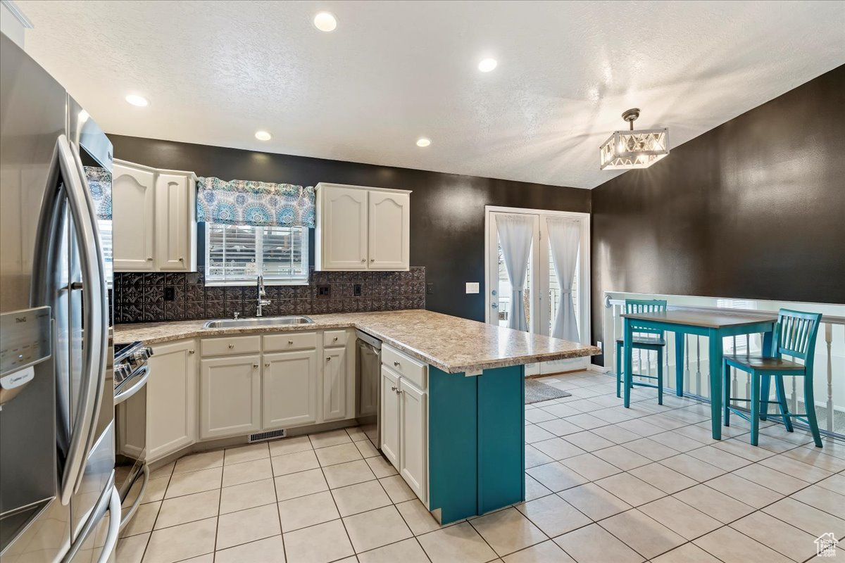 Kitchen with kitchen peninsula, appliances with stainless steel finishes, sink, white cabinetry, and light tile patterned flooring