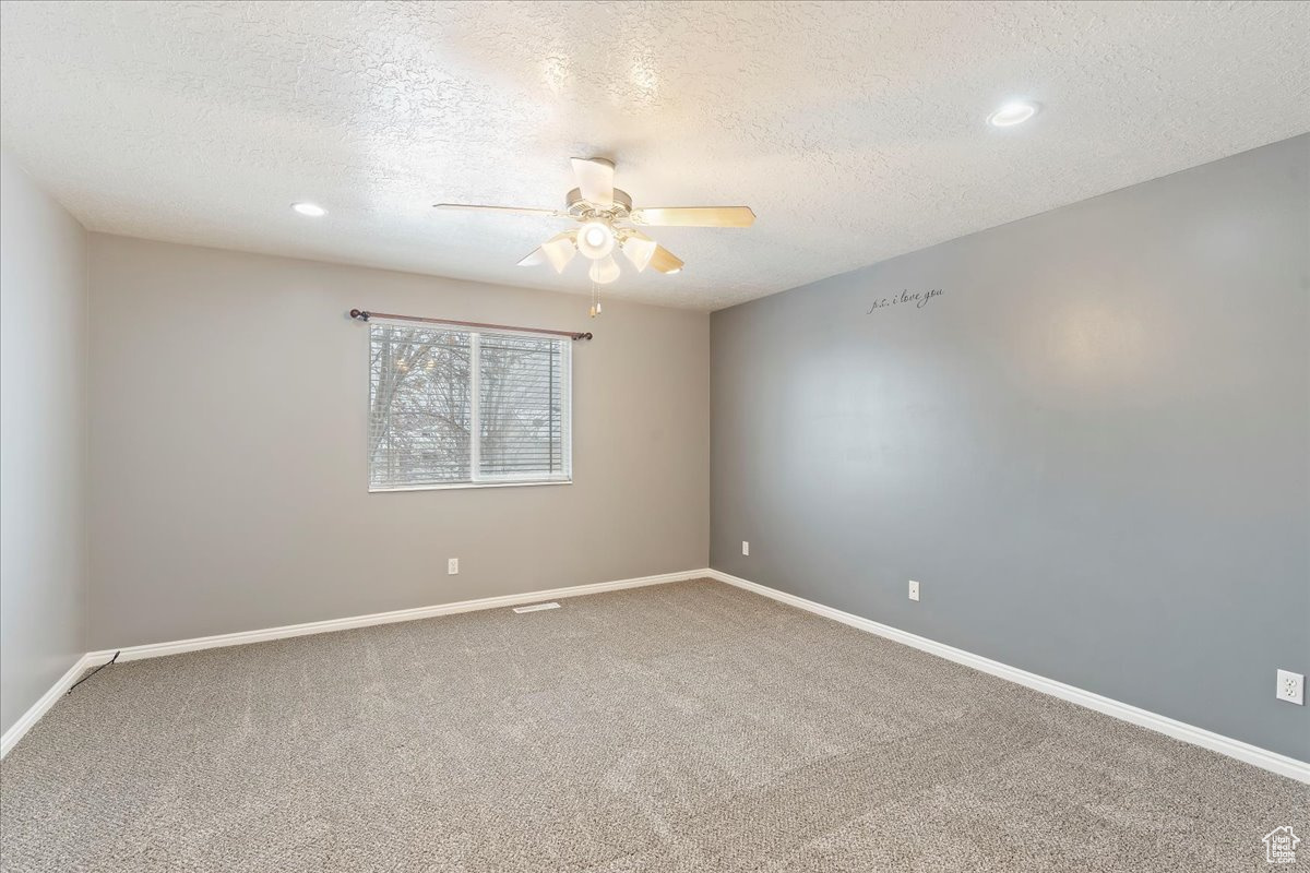 Carpeted empty room featuring a textured ceiling and ceiling fan