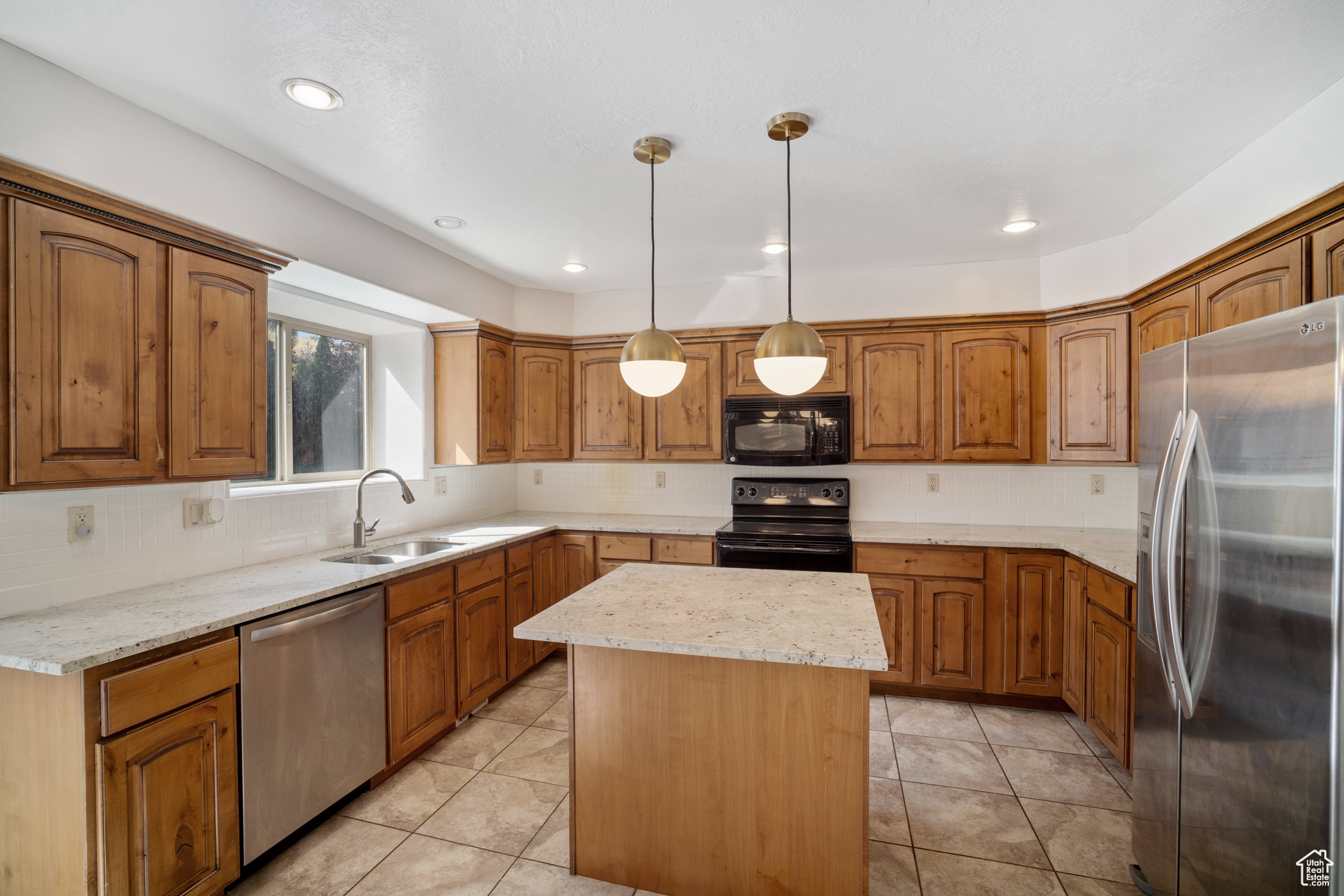 Kitchen featuring a center island, sink, backsplash, decorative light fixtures, and black appliances