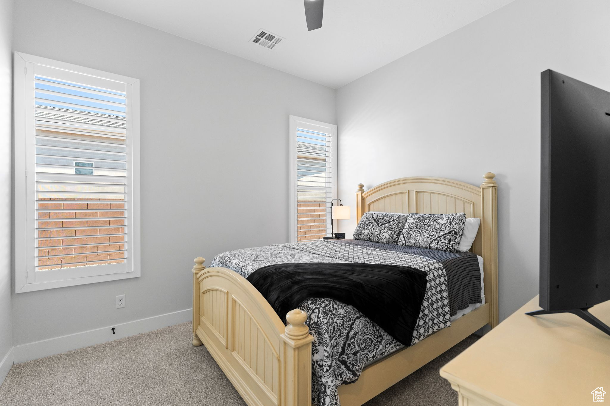 Bedroom featuring light carpet and ceiling fan and plantation shutters.