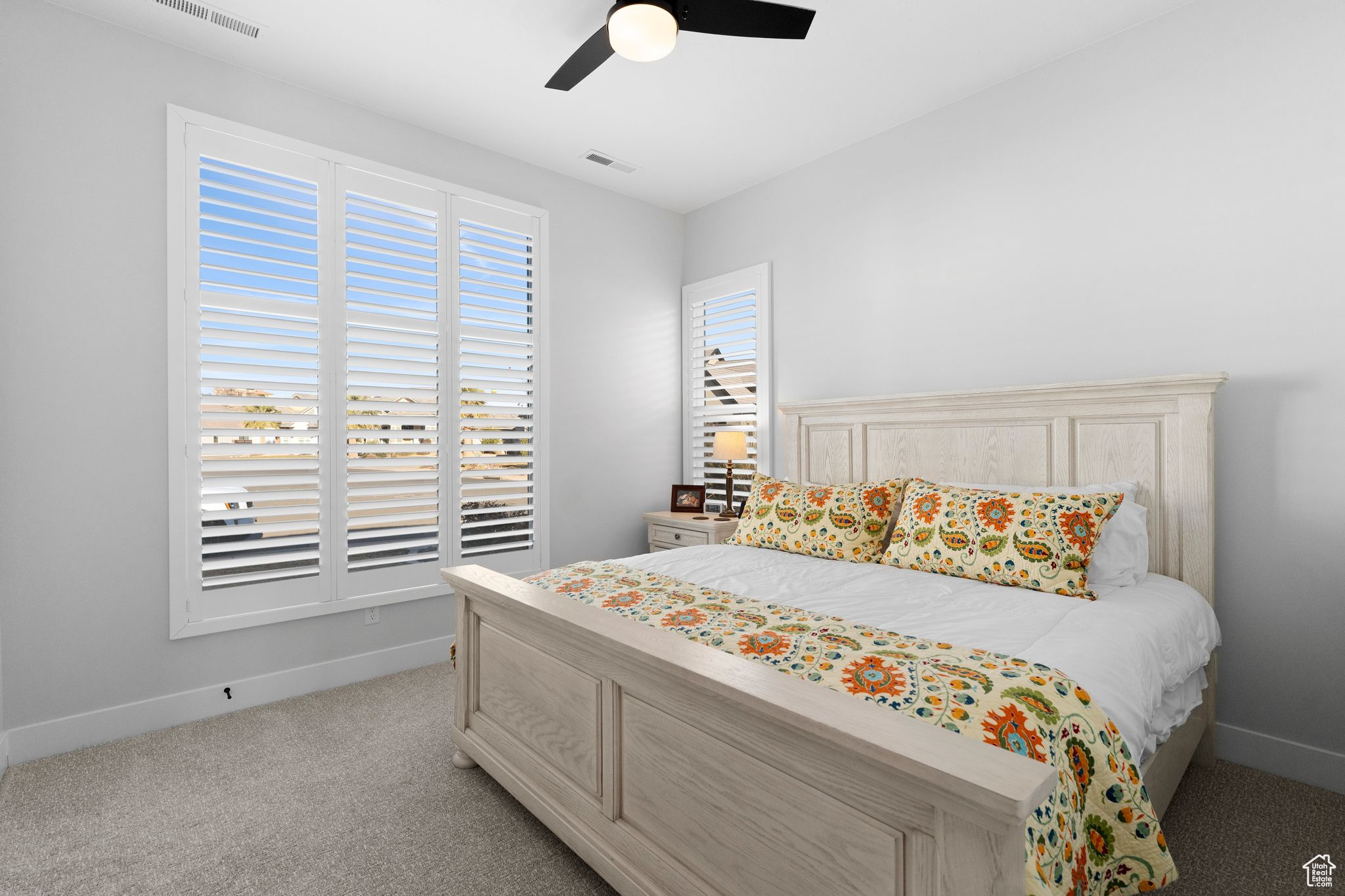 Bedroom with light colored carpet and ceiling fan, plantation shutters & views.