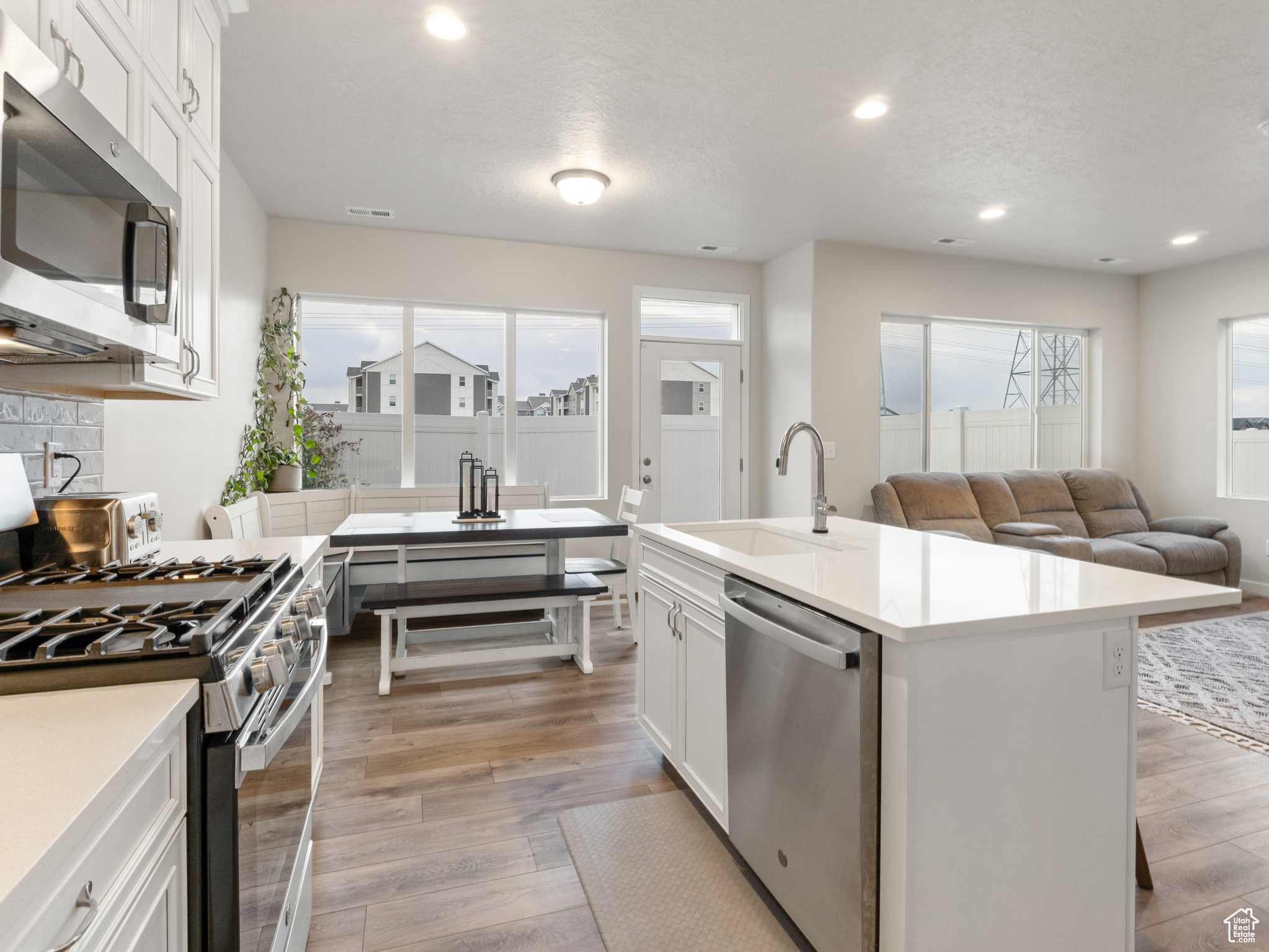 Kitchen featuring sink, white cabinets, stainless steel appliances, and a center island with sink