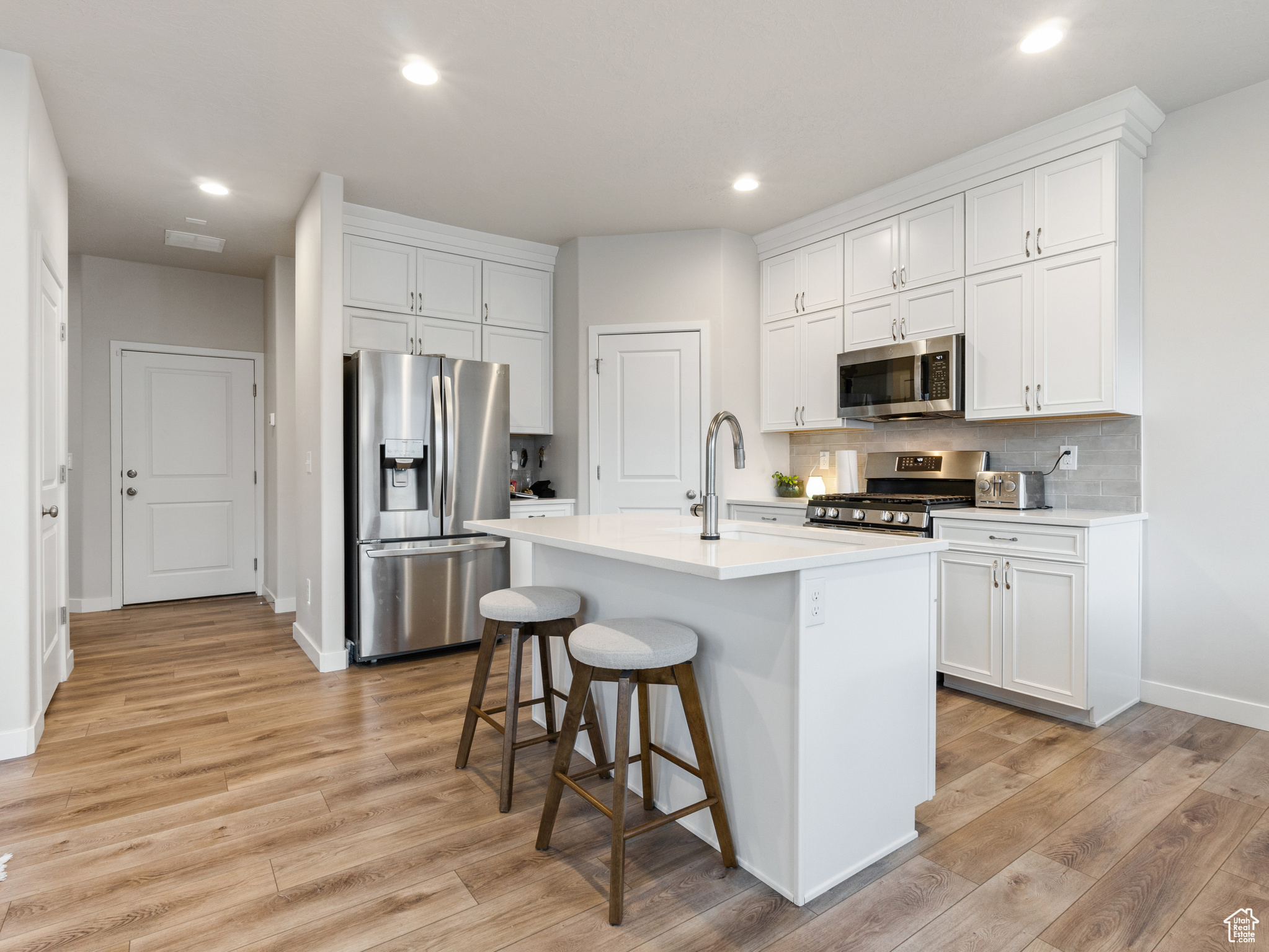 Kitchen featuring a breakfast bar area, a kitchen island with sink, white cabinets, and appliances with stainless steel finishes