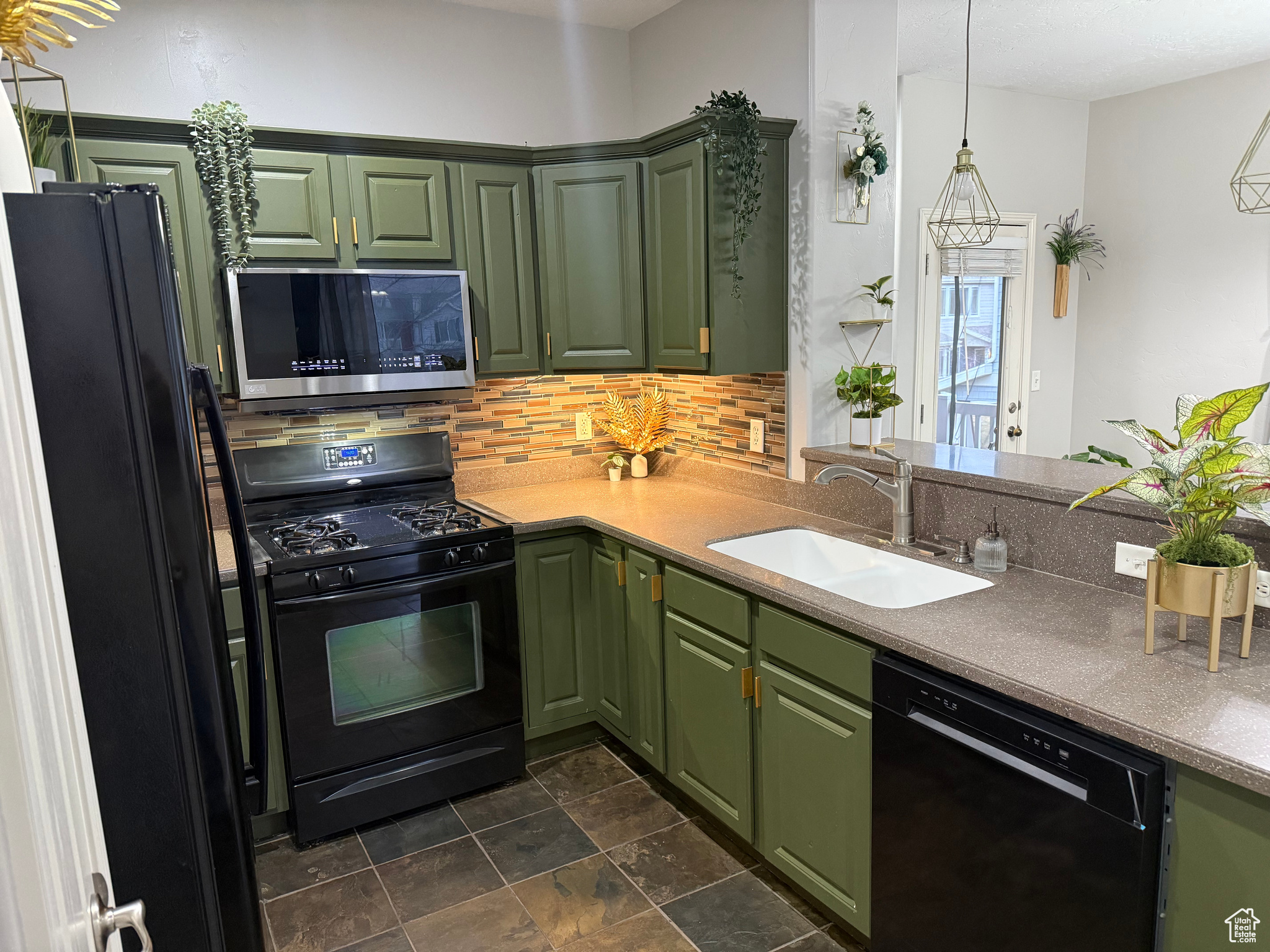 Kitchen with kitchen peninsula, decorative backsplash, sink, black appliances, and green cabinetry