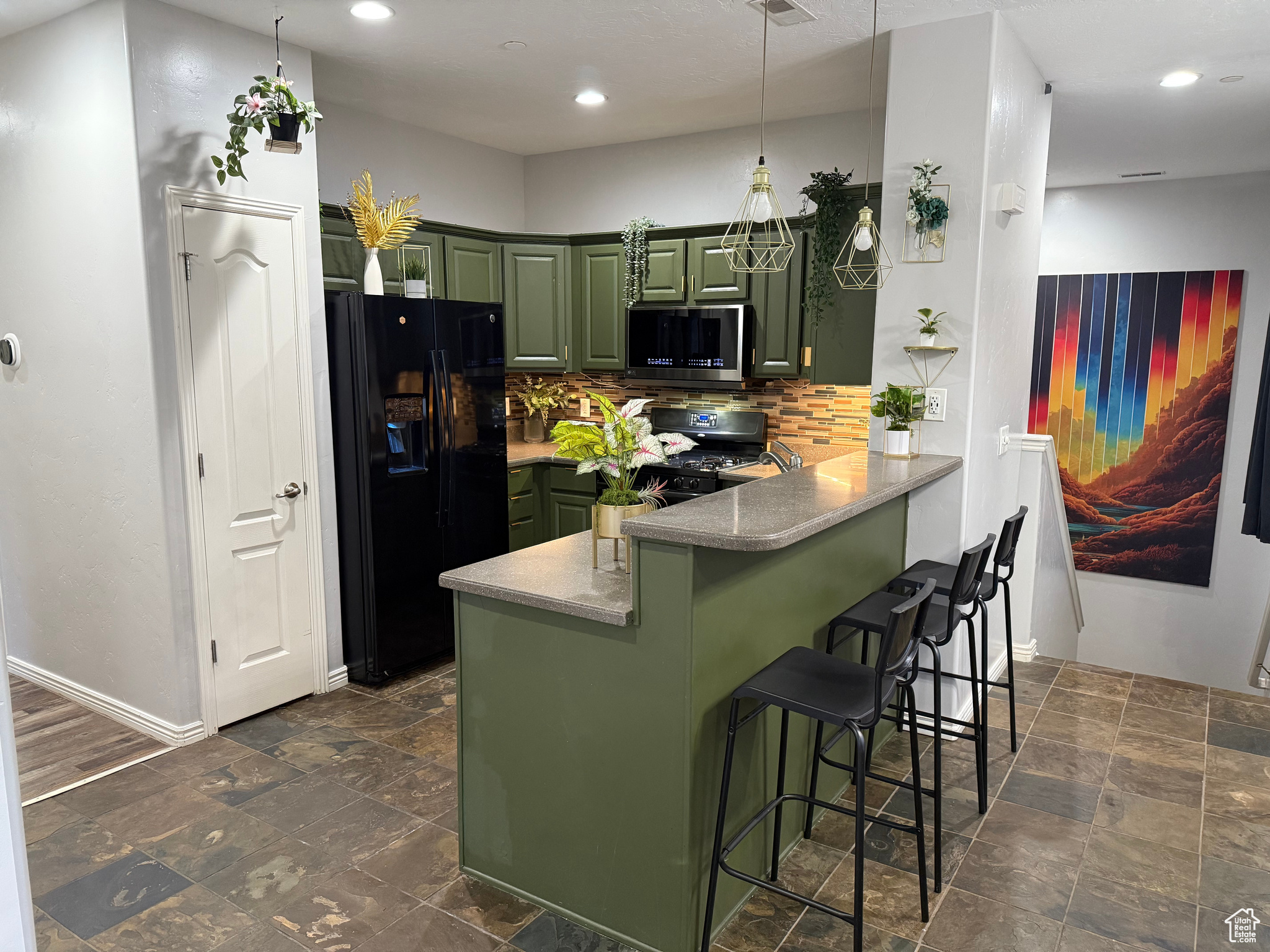 Kitchen with black appliances, green cabinetry, tasteful backsplash, kitchen peninsula, and a breakfast bar area