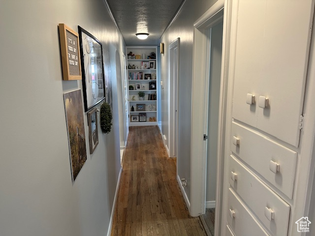 Hall featuring built in shelves, a textured ceiling, and dark hardwood / wood-style flooring