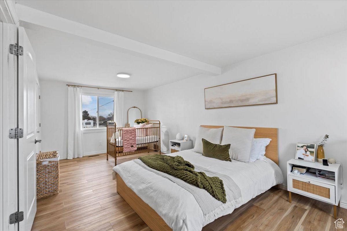 Bedroom with beamed ceiling and light wood-type flooring