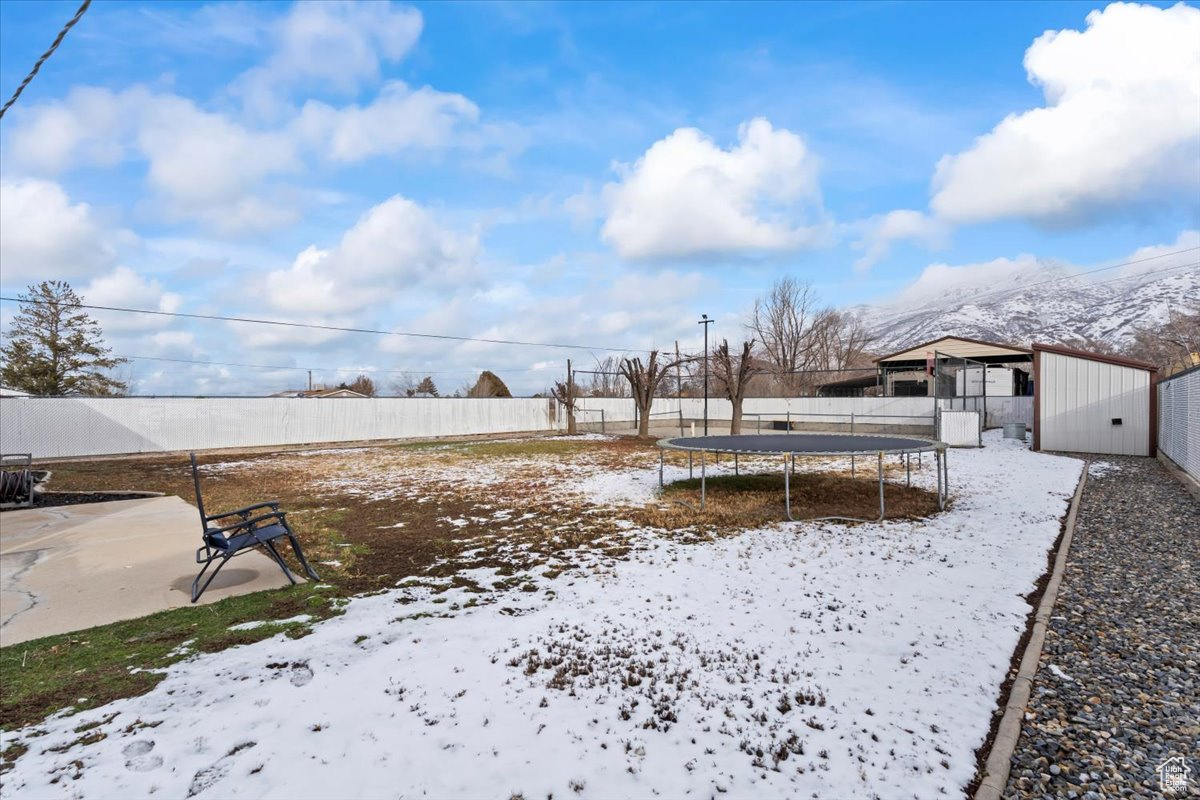 Yard covered in snow featuring an outbuilding and a trampoline