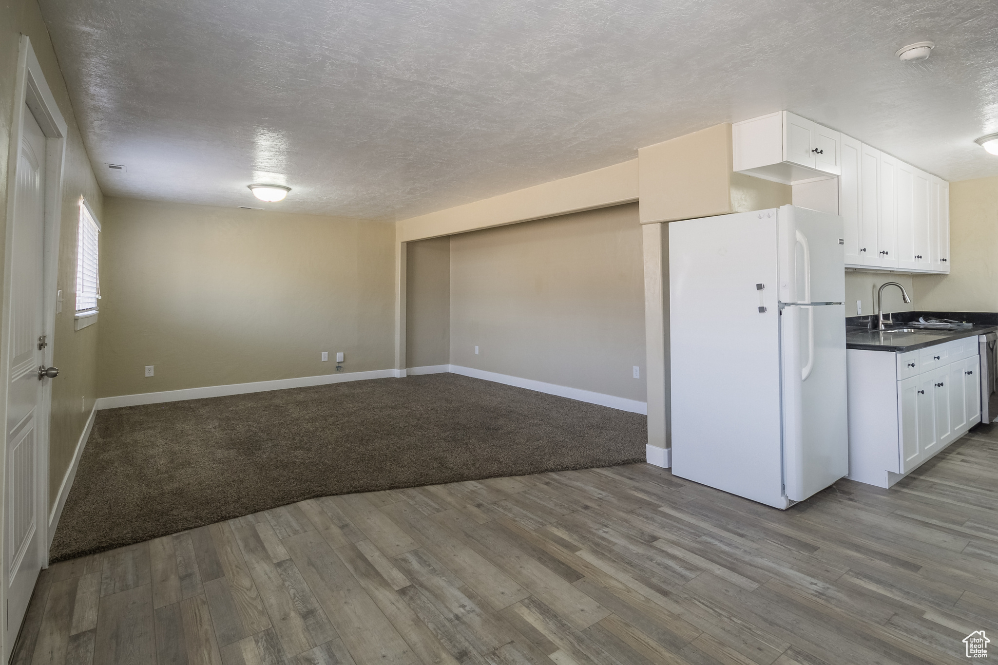 Kitchen featuring a textured ceiling, sink, light hardwood / wood-style flooring, white cabinets, and white fridge