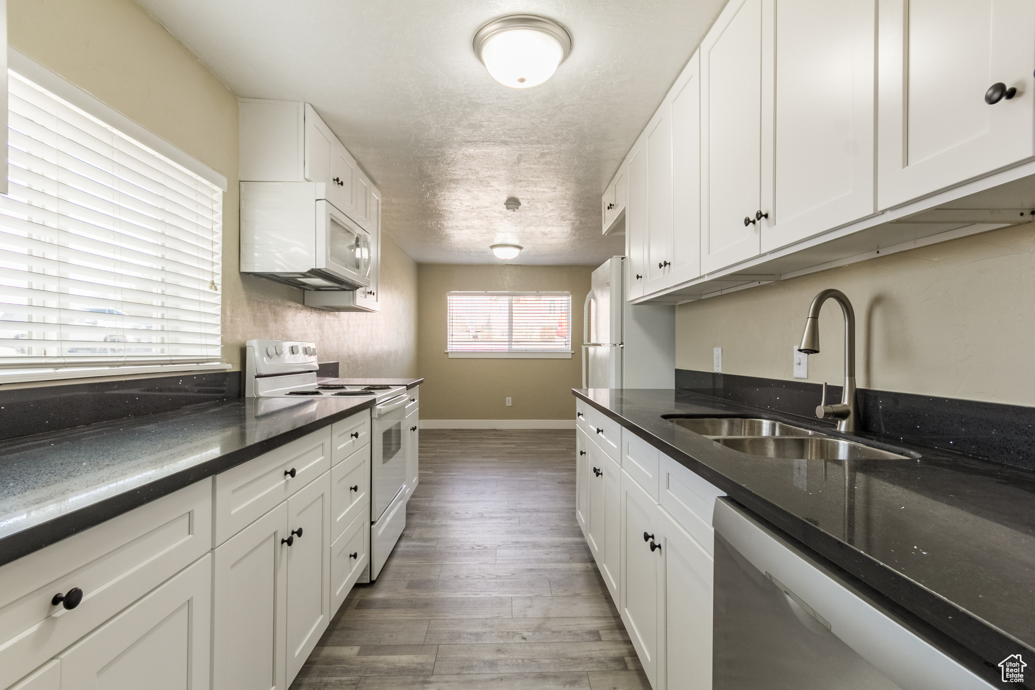 Kitchen featuring white appliances, dark hardwood / wood-style floors, white cabinetry, and sink