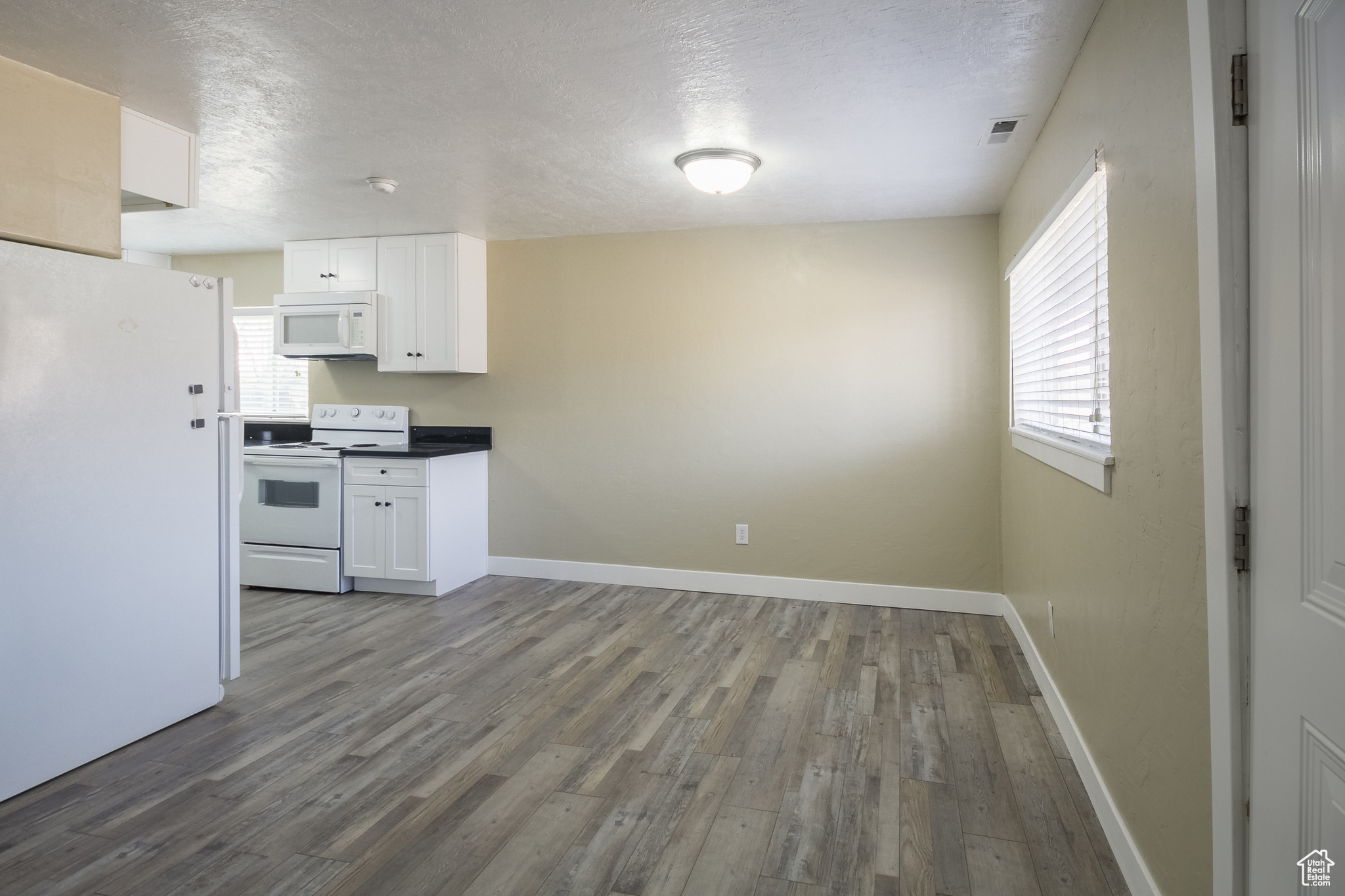 Kitchen with a textured ceiling, white cabinets, wood-type flooring, and white appliances