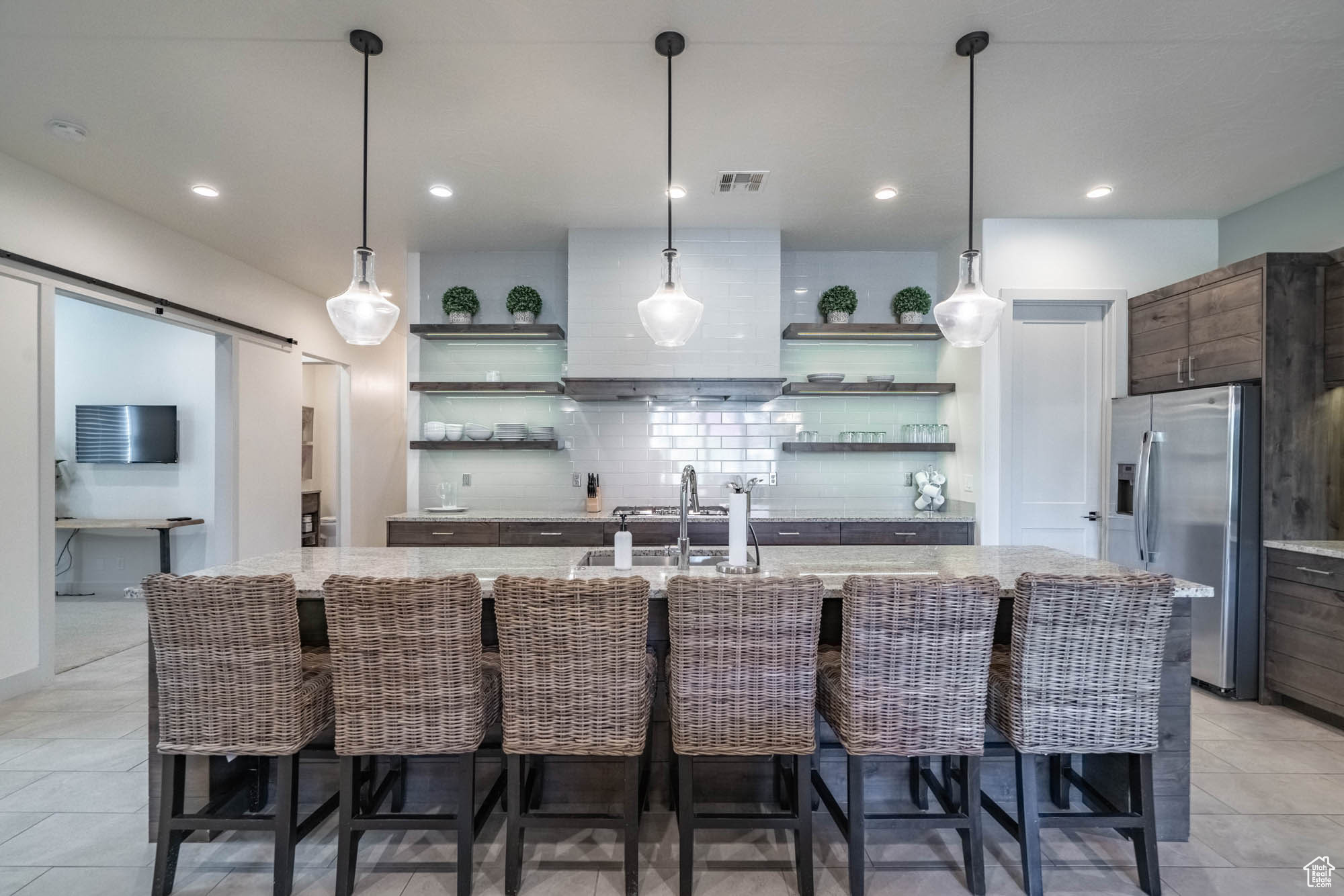 Kitchen featuring pendant lighting, backsplash, a kitchen island with sink, stainless steel fridge, and a breakfast bar area