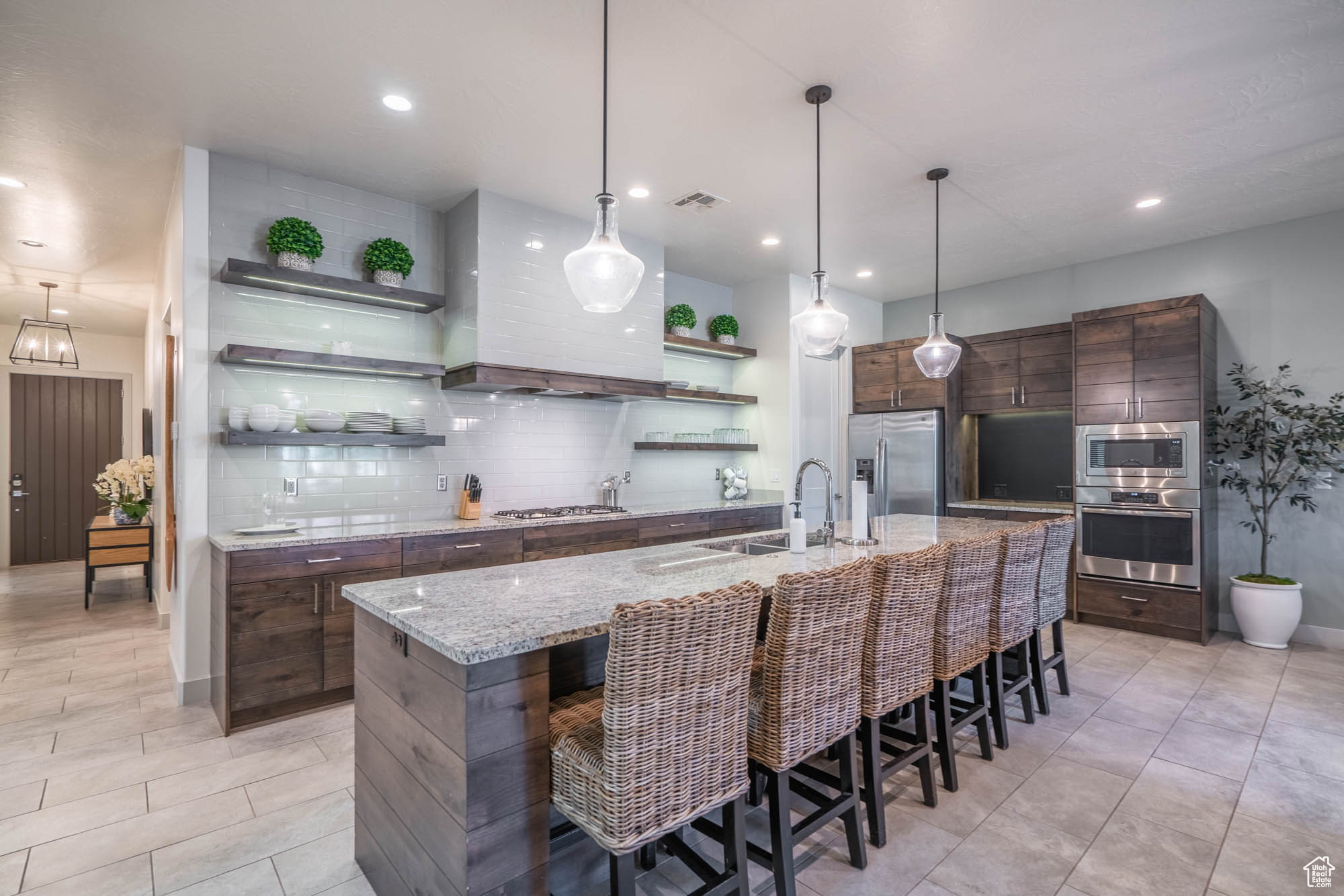 Kitchen featuring a kitchen bar, dark brown cabinetry, stainless steel appliances, a kitchen island with sink, and decorative light fixtures