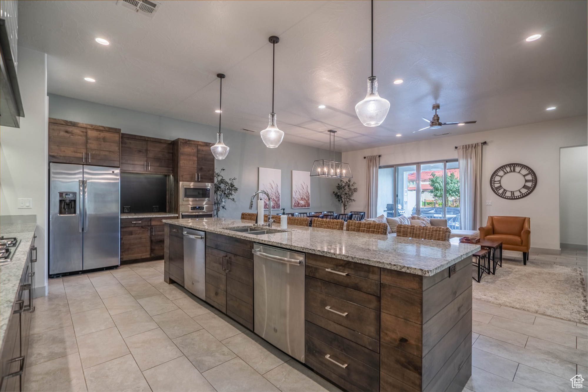 Kitchen featuring appliances with stainless steel finishes, ceiling fan with notable chandelier, sink, hanging light fixtures, and a large island