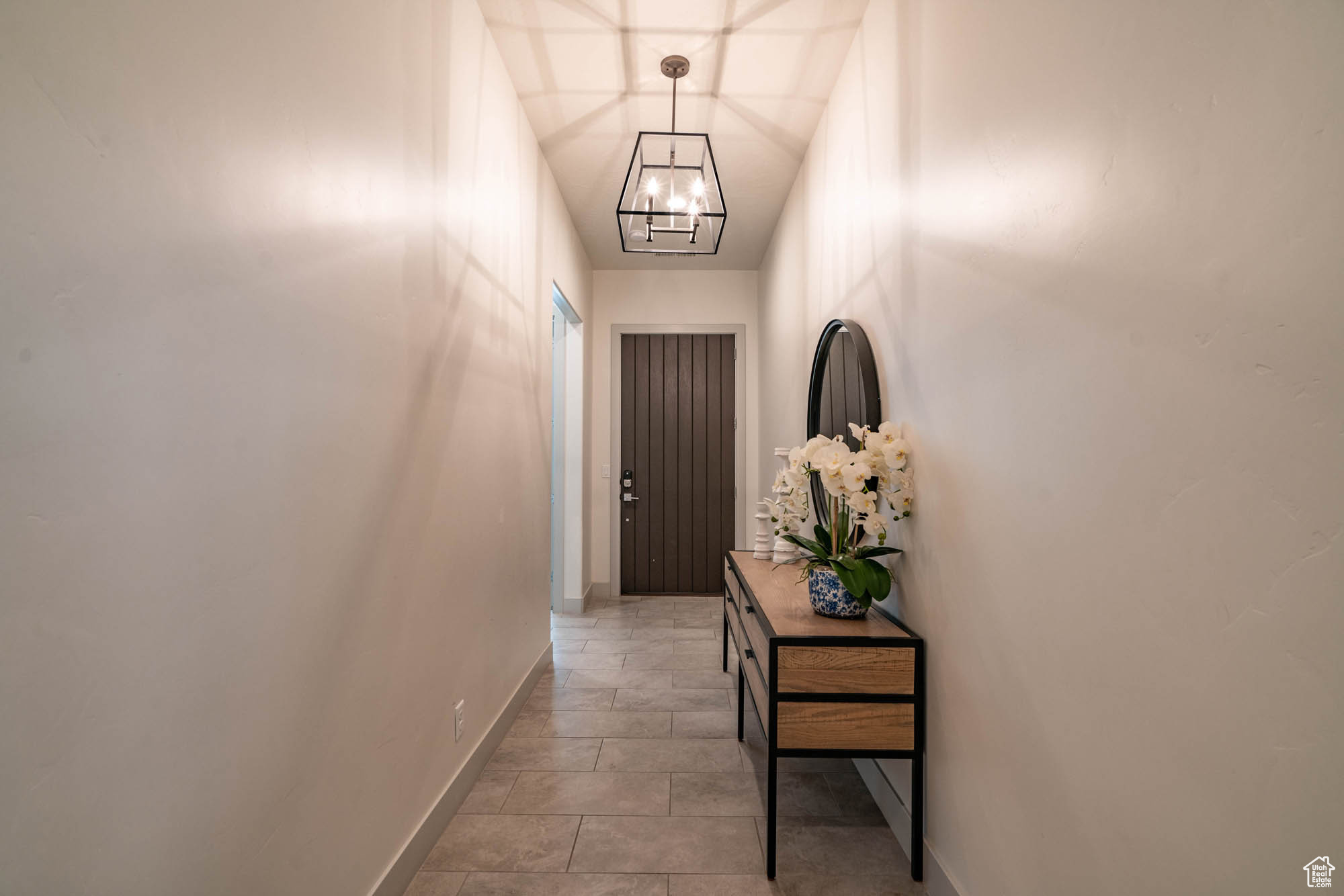 Corridor featuring lofted ceiling, a notable chandelier, and light tile patterned flooring