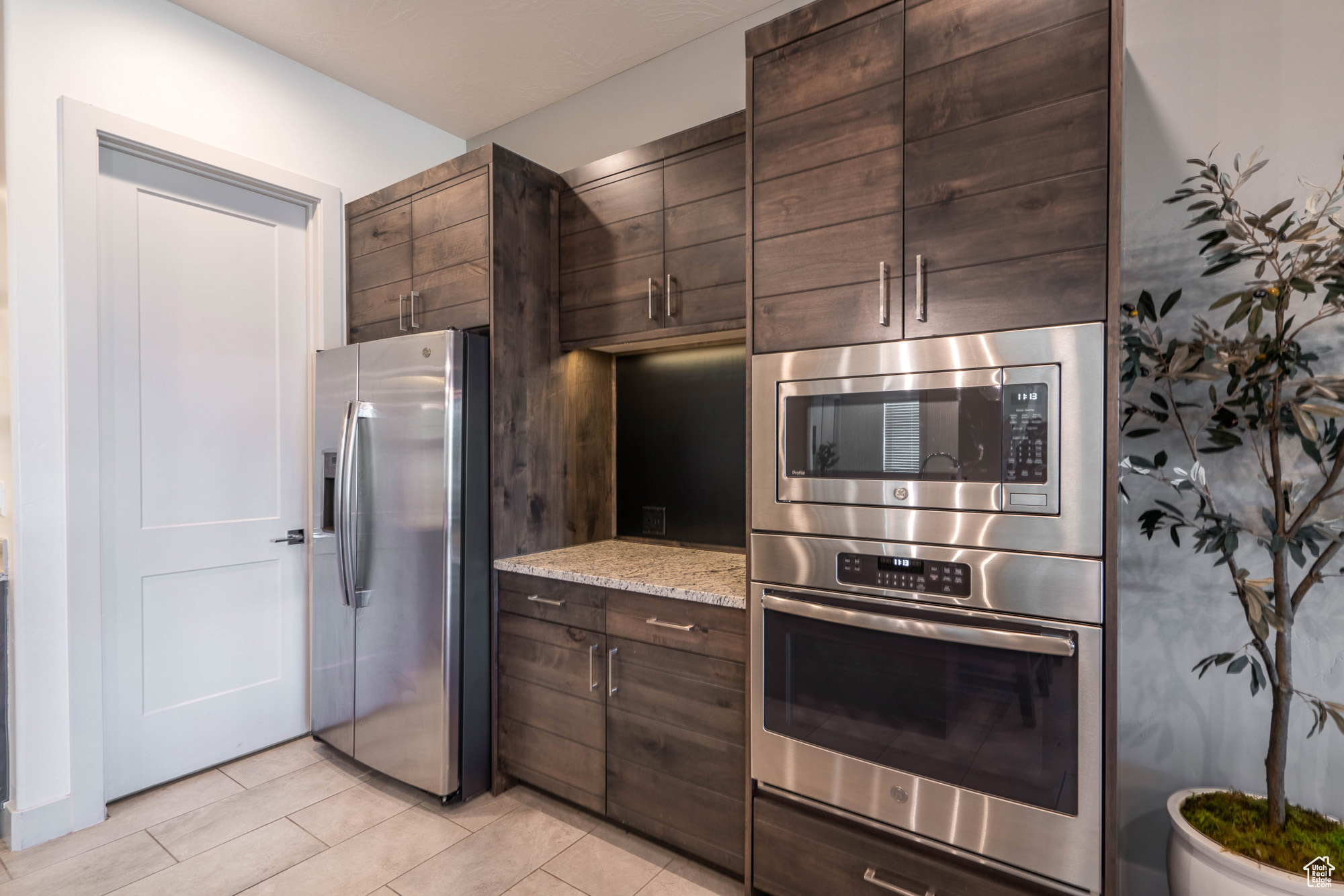 Kitchen with light stone countertops, dark brown cabinetry, and stainless steel appliances