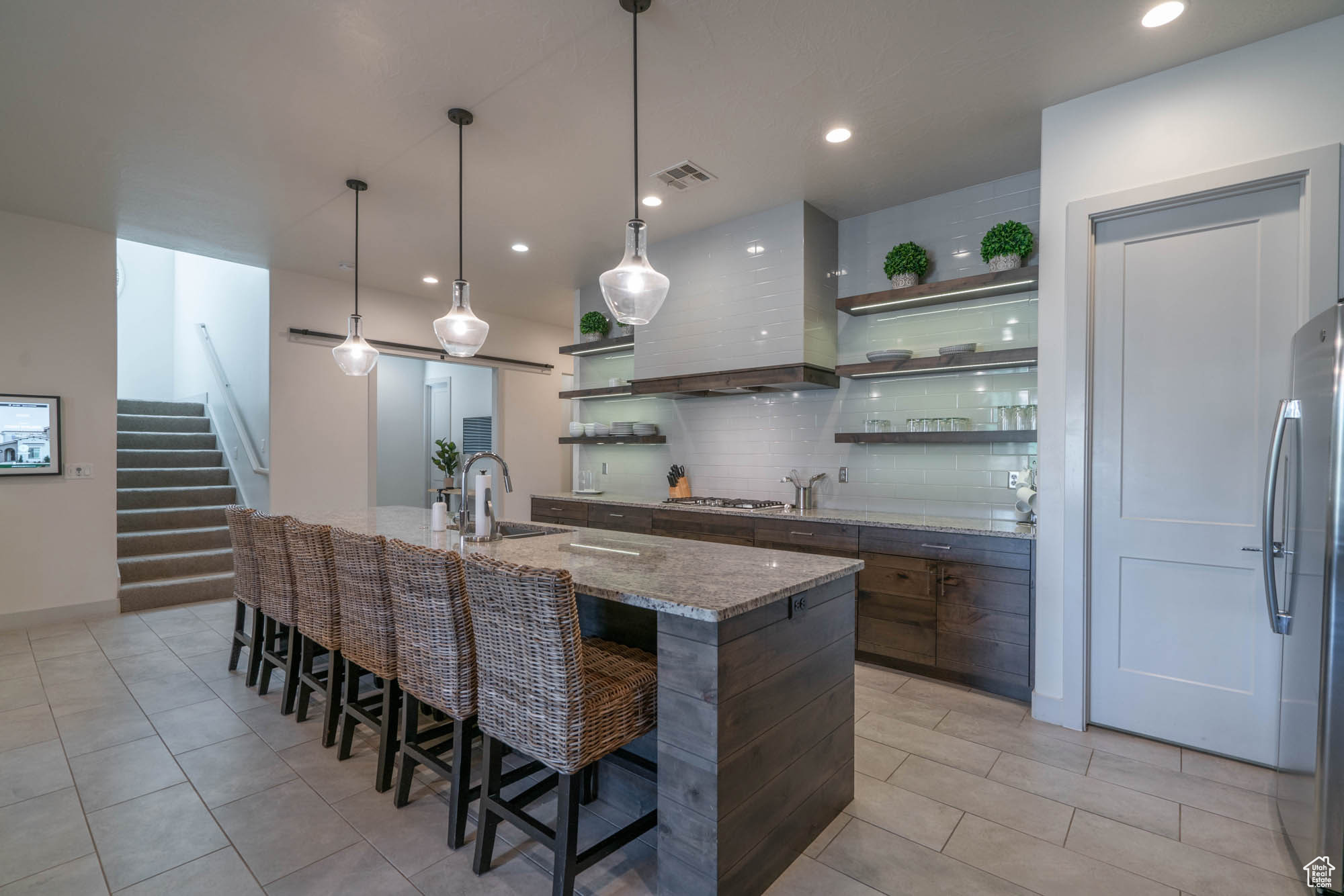 Kitchen featuring a kitchen island with sink, sink, light stone counters, a kitchen bar, and custom range hood