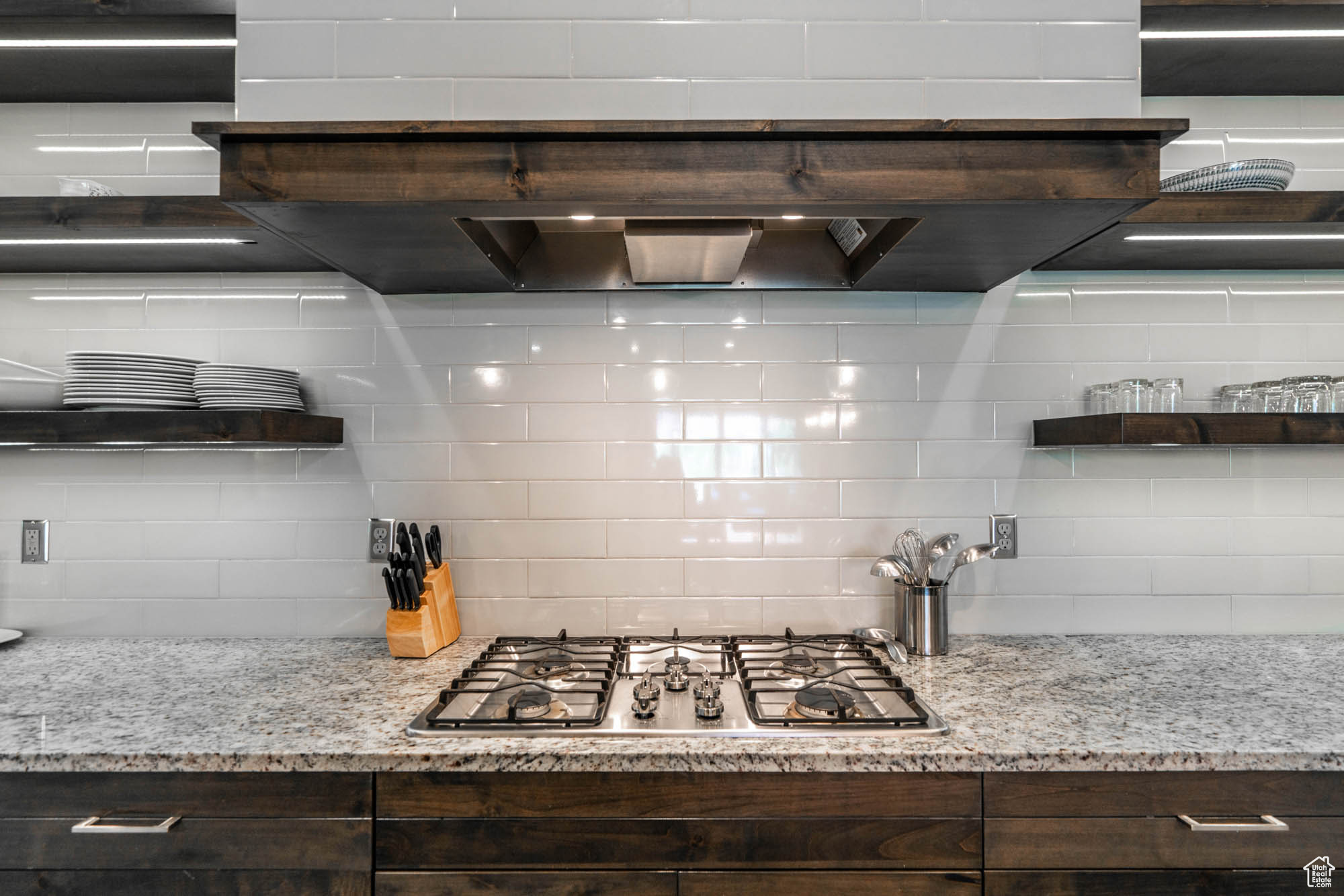 Kitchen with decorative backsplash, dark brown cabinetry, stainless steel gas cooktop, and light stone countertops