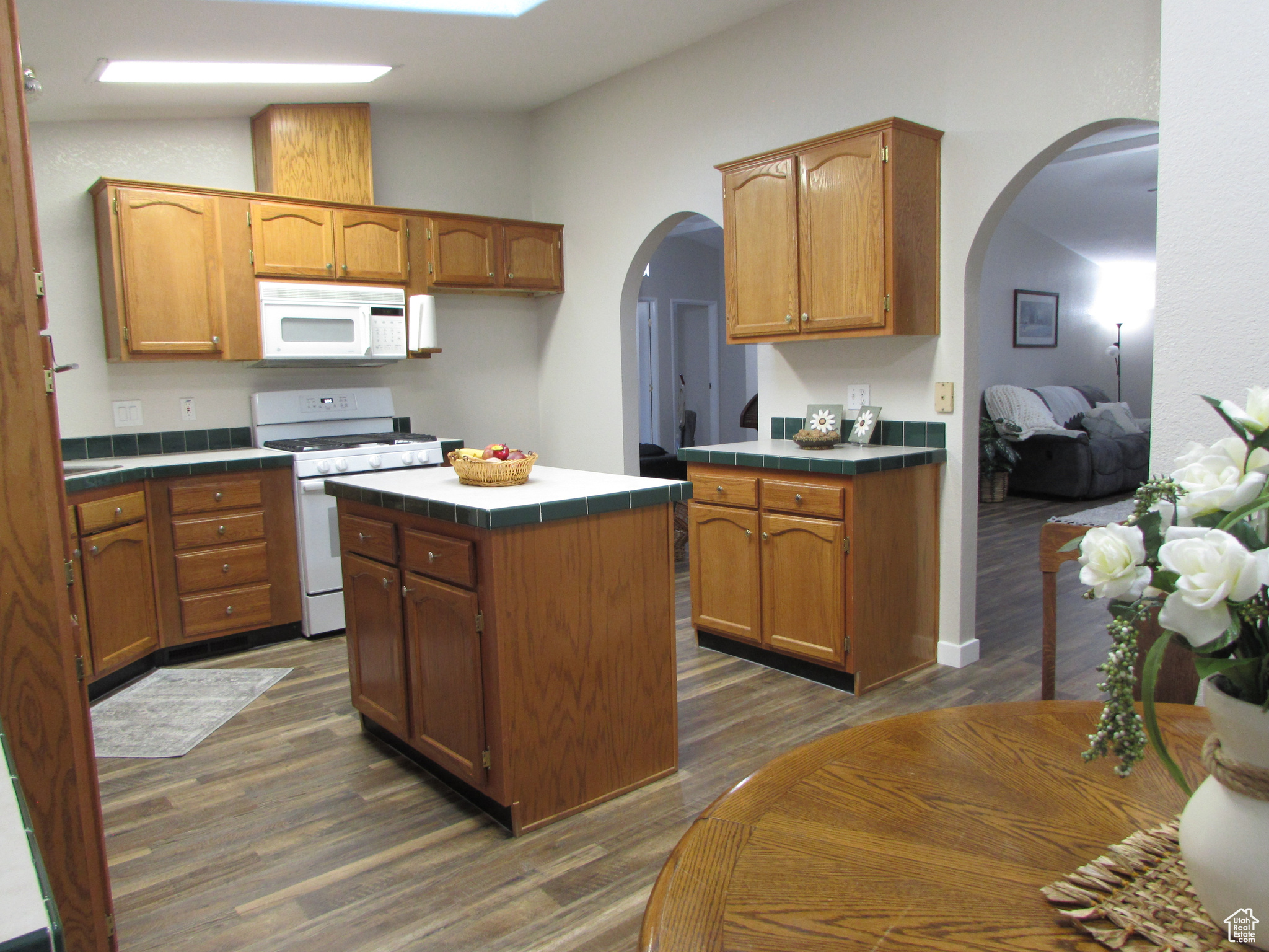 Kitchen with tile edged counters, a center island, dark hardwood / wood-style floors, and white appliances