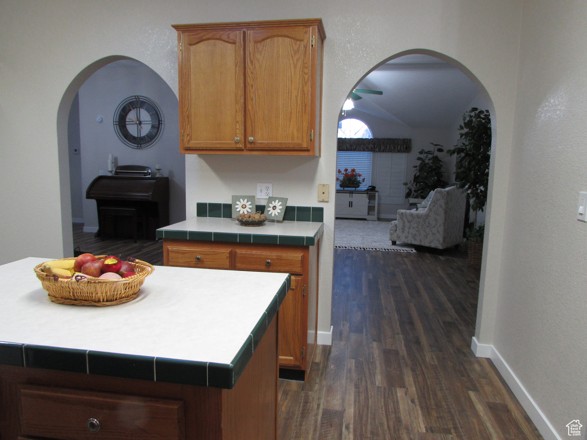 Kitchen looking into living room area featuring tile edged counters, dark hardwood / wood-style flooring, a kitchen island, and lofted ceiling