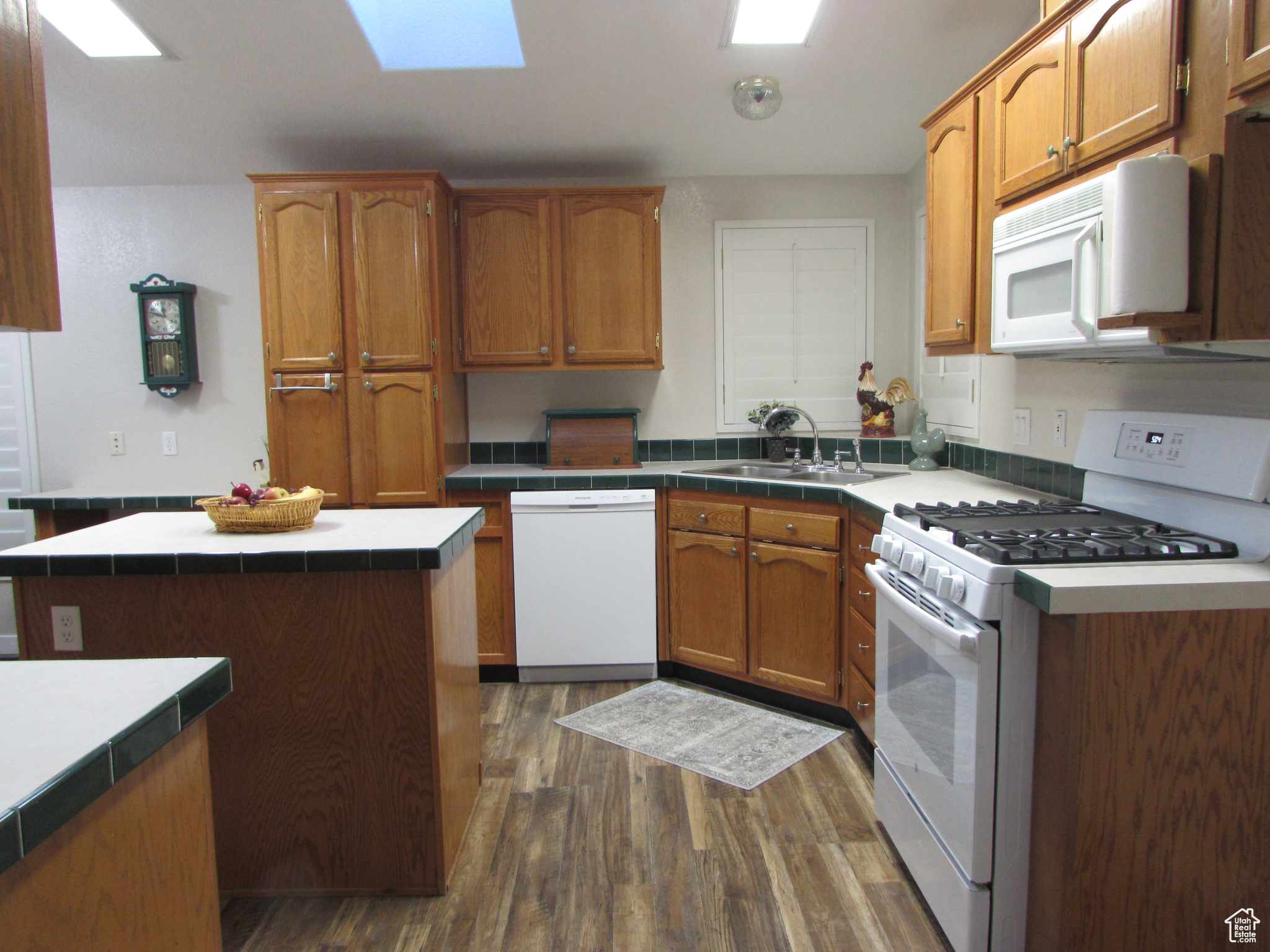 Kitchen with white appliances, sink, a skylight, a kitchen island, and dark hardwood / wood-style flooring