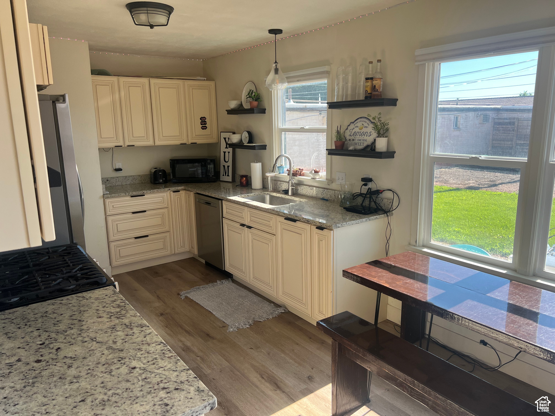 Kitchen featuring sink, hanging light fixtures, light wood-type flooring, light stone counters, and stainless steel appliances