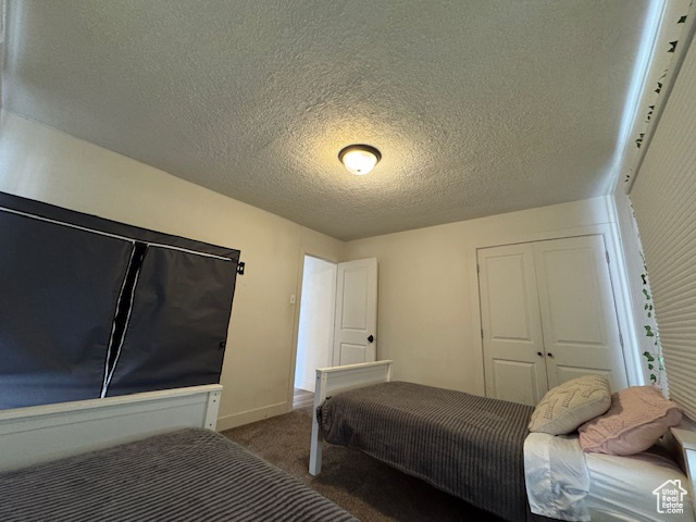 Bedroom with a textured ceiling, dark carpet, and a closet