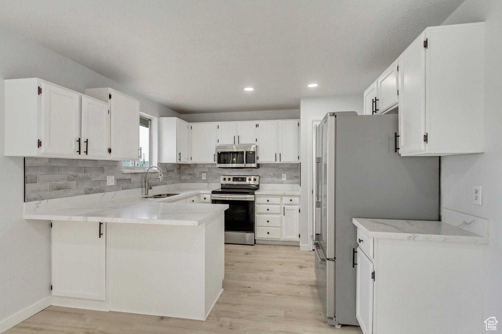 Kitchen featuring decorative backsplash, kitchen peninsula, stainless steel appliances, sink, and white cabinets