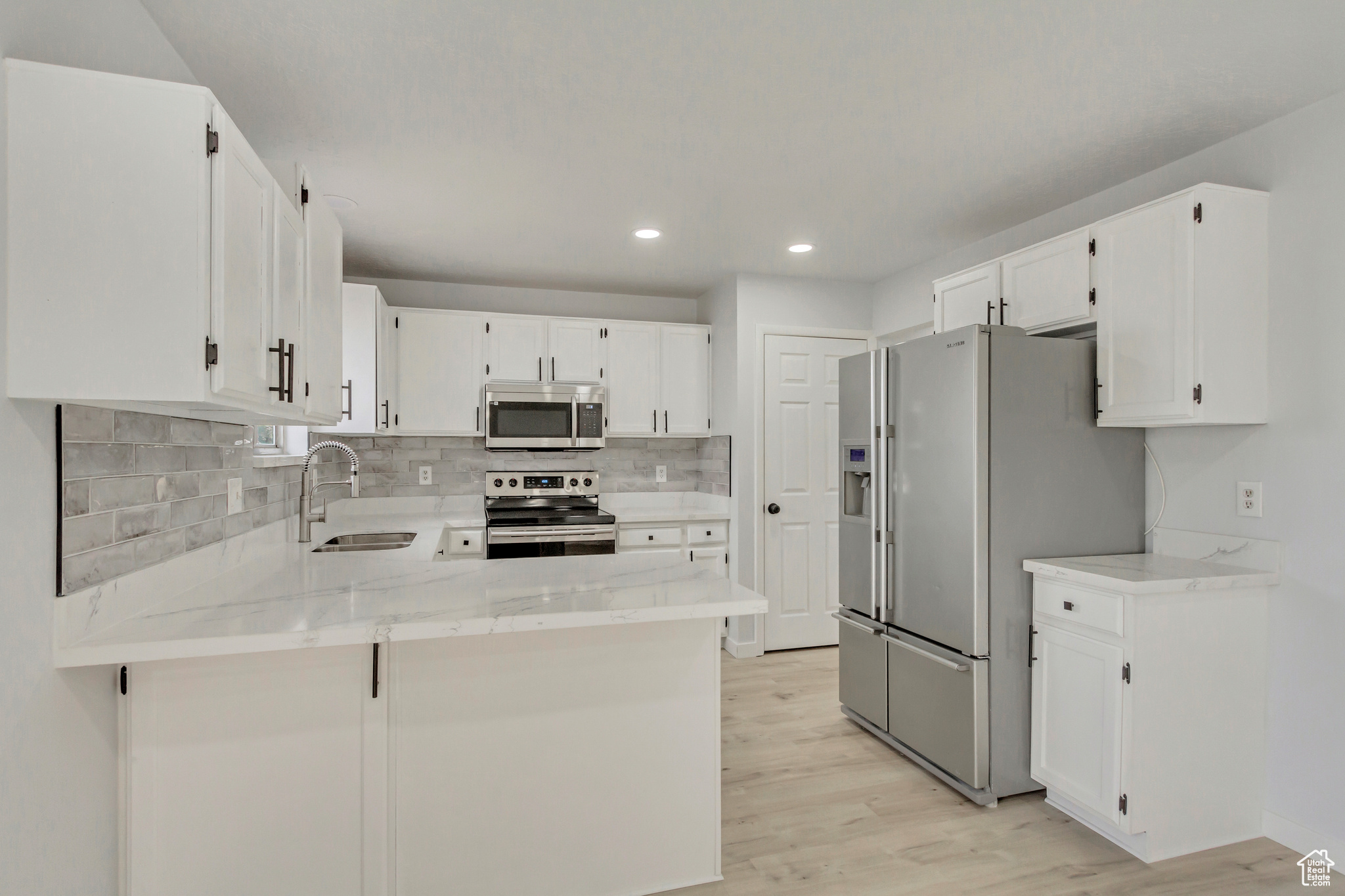 Kitchen with kitchen peninsula, sink, light hardwood / wood-style flooring, appliances with stainless steel finishes, and white cabinetry