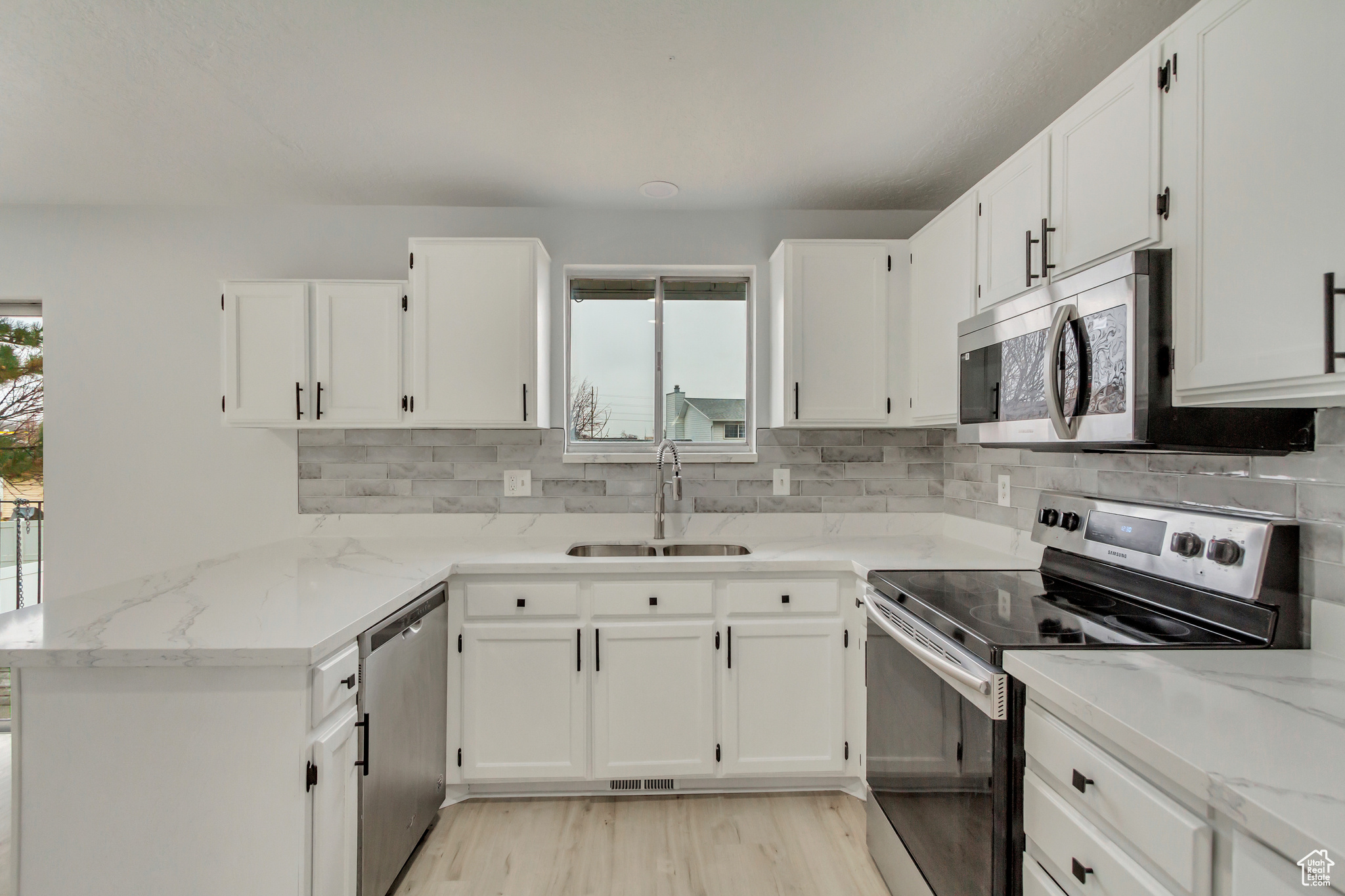 Kitchen with light stone countertops, white cabinetry, sink, and stainless steel appliances