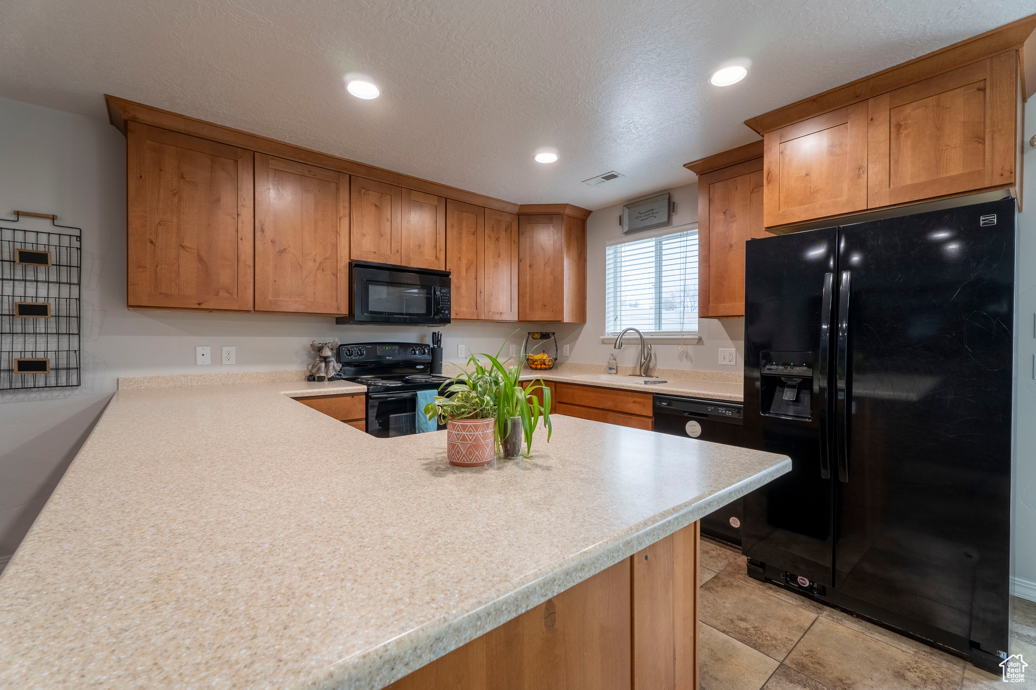 Kitchen with black appliances, kitchen peninsula, sink, and a textured ceiling