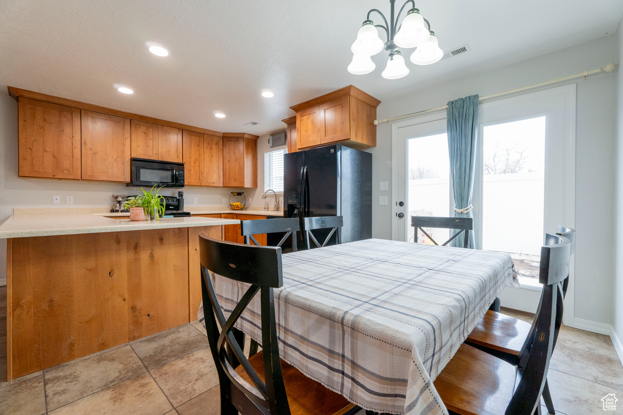 Kitchen featuring kitchen peninsula, sink, black appliances, a chandelier, and hanging light fixtures