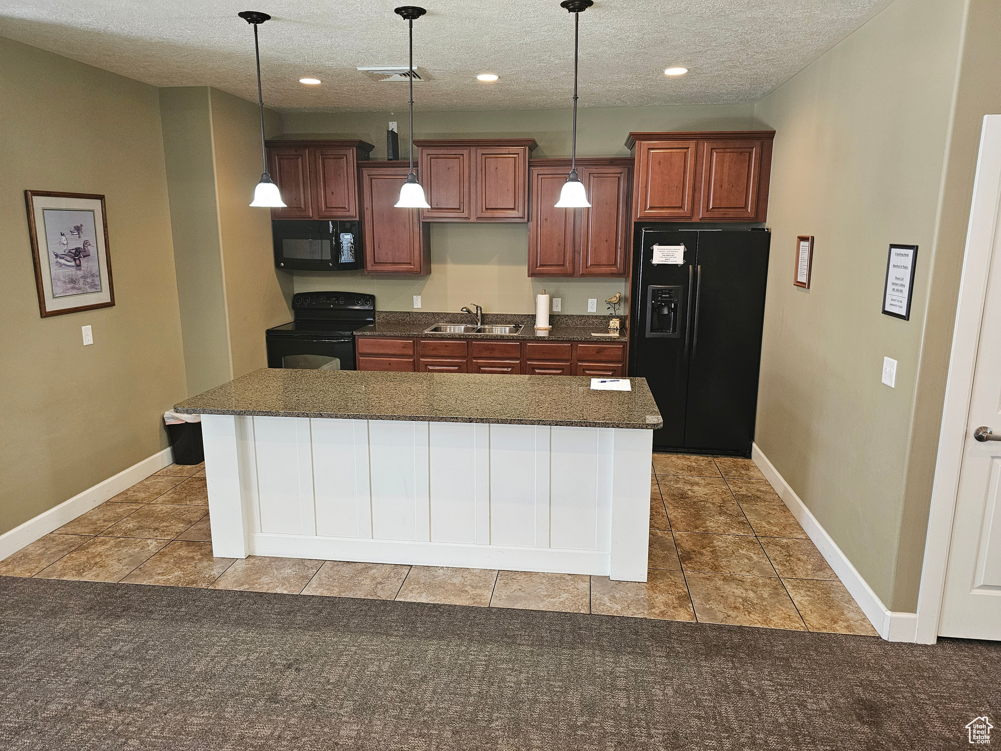 Kitchen with a textured ceiling, black appliances, decorative light fixtures, tile patterned flooring, and a kitchen island