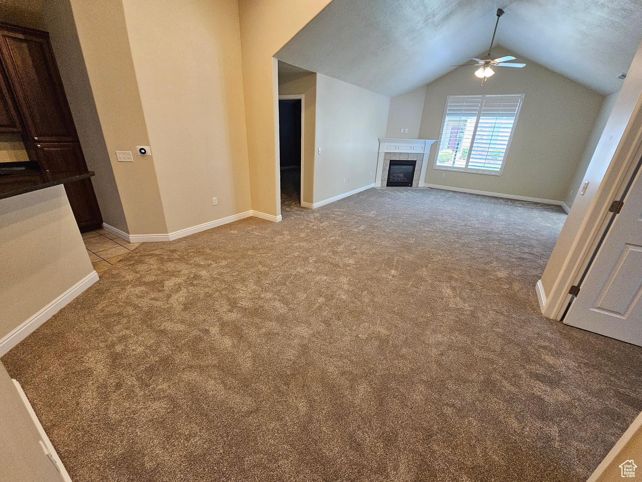 Unfurnished living room featuring ceiling fan, light colored carpet, a fireplace, and vaulted ceiling