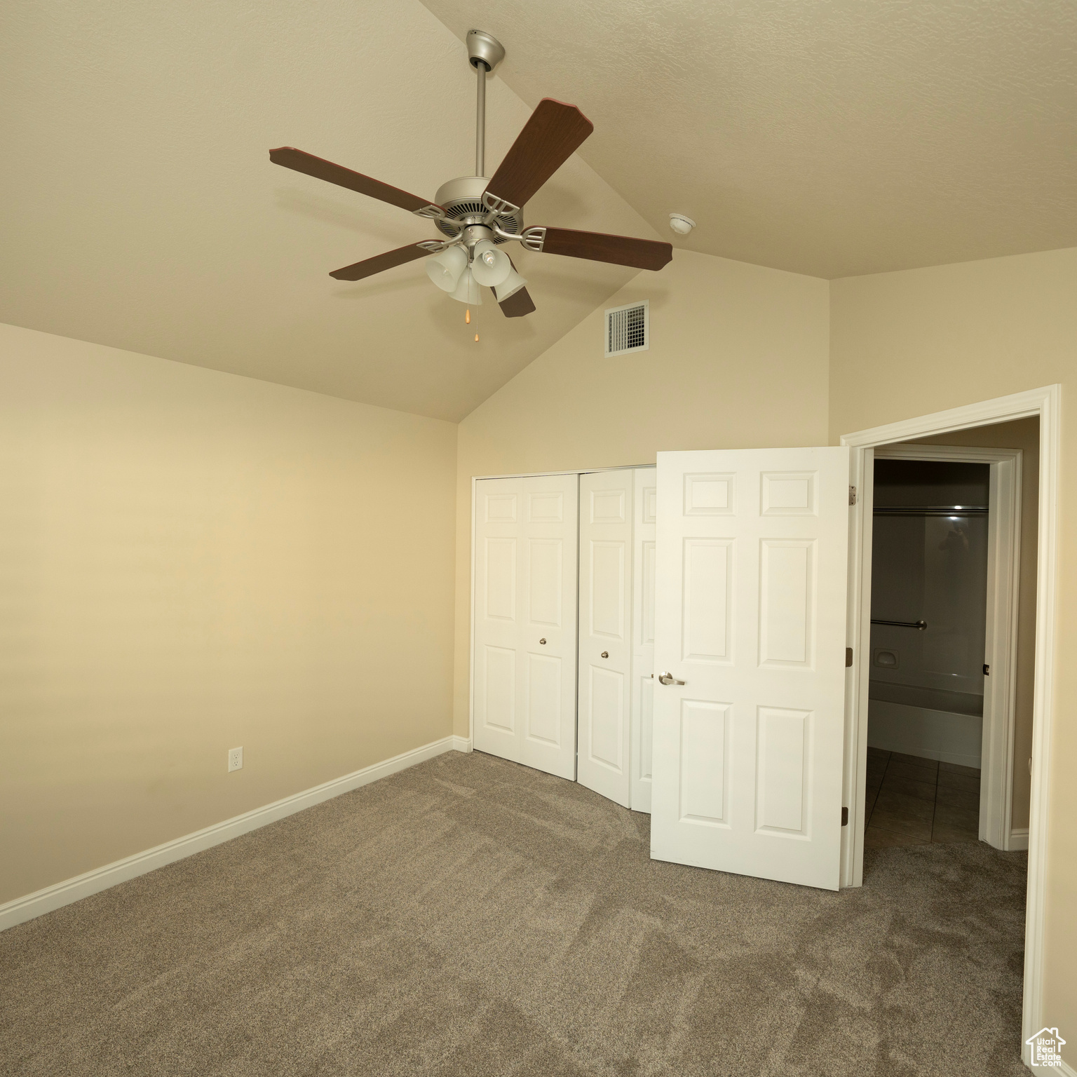 Unfurnished bedroom featuring ceiling fan, dark carpet, vaulted ceiling, and a closet