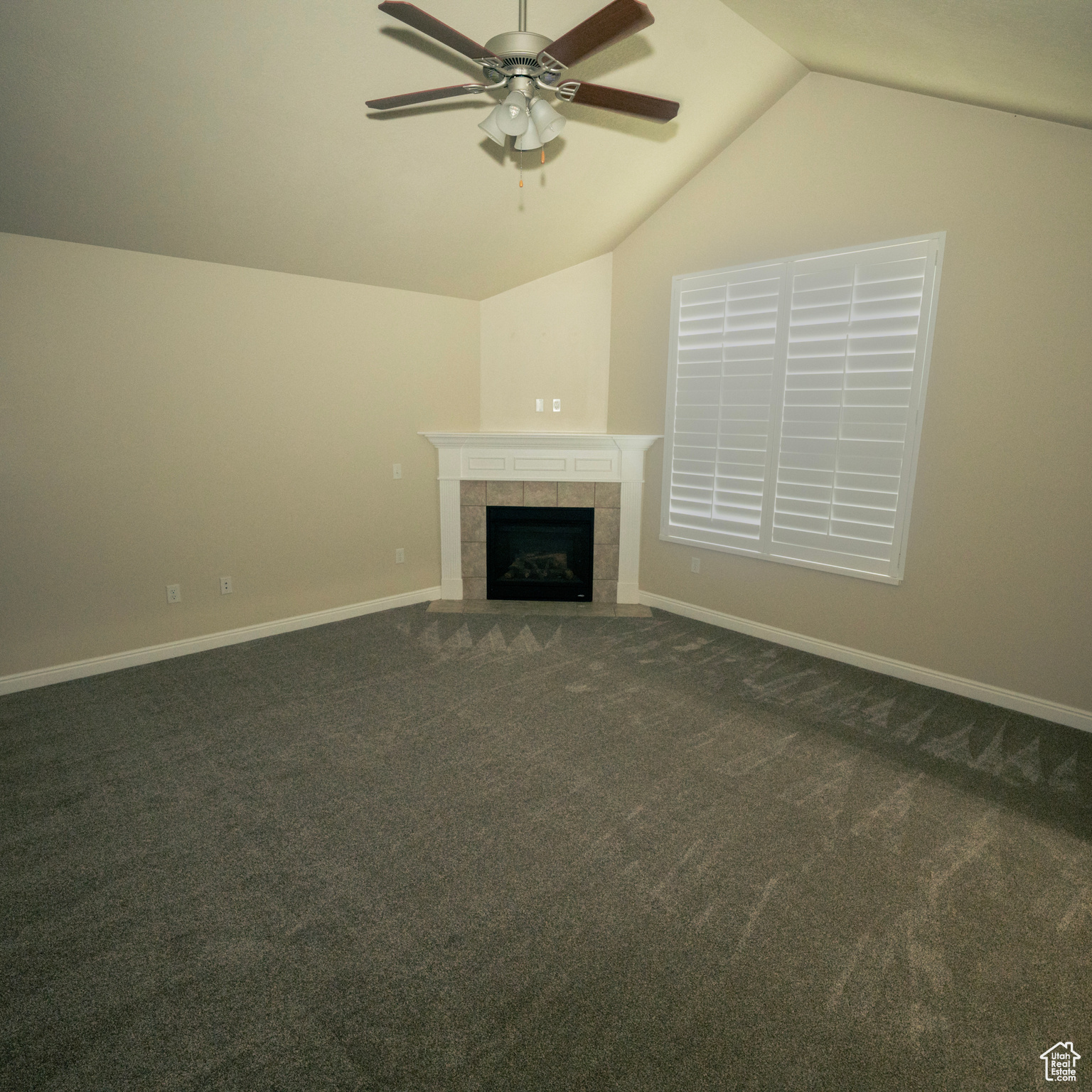 Unfurnished living room featuring dark colored carpet, ceiling fan, a tile fireplace, and vaulted ceiling