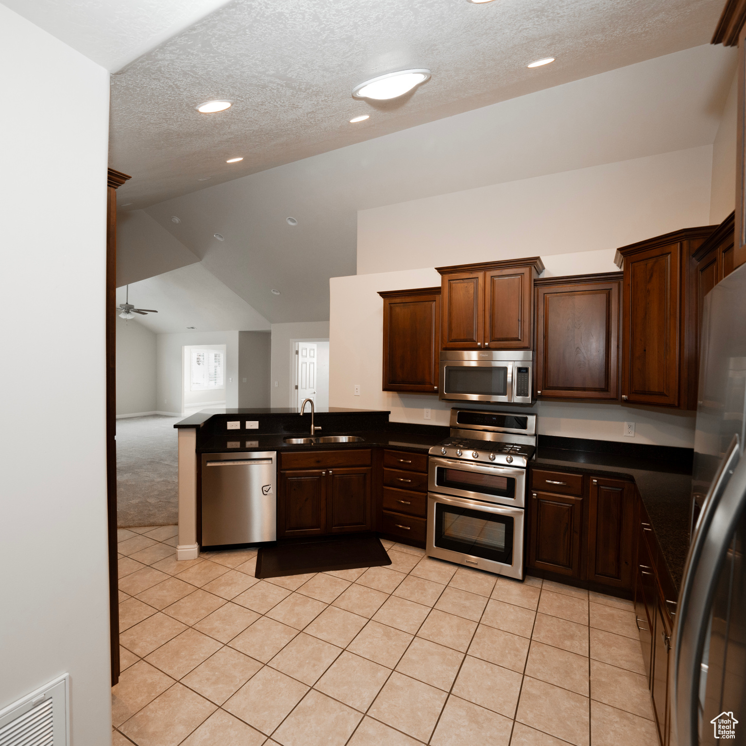 Kitchen featuring ceiling fan, sink, vaulted ceiling, light tile patterned flooring, and appliances with stainless steel finishes