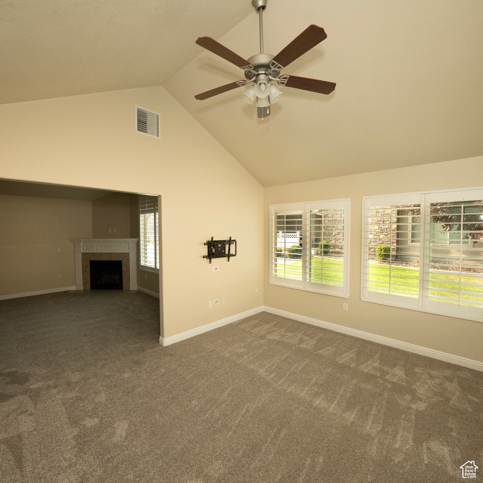 Unfurnished living room featuring vaulted ceiling, dark carpet, ceiling fan, and a tiled fireplace