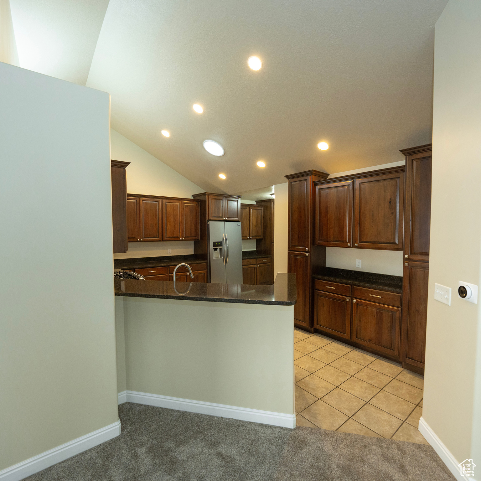 Kitchen with kitchen peninsula, light tile patterned floors, dark stone counters, and stainless steel refrigerator with ice dispenser