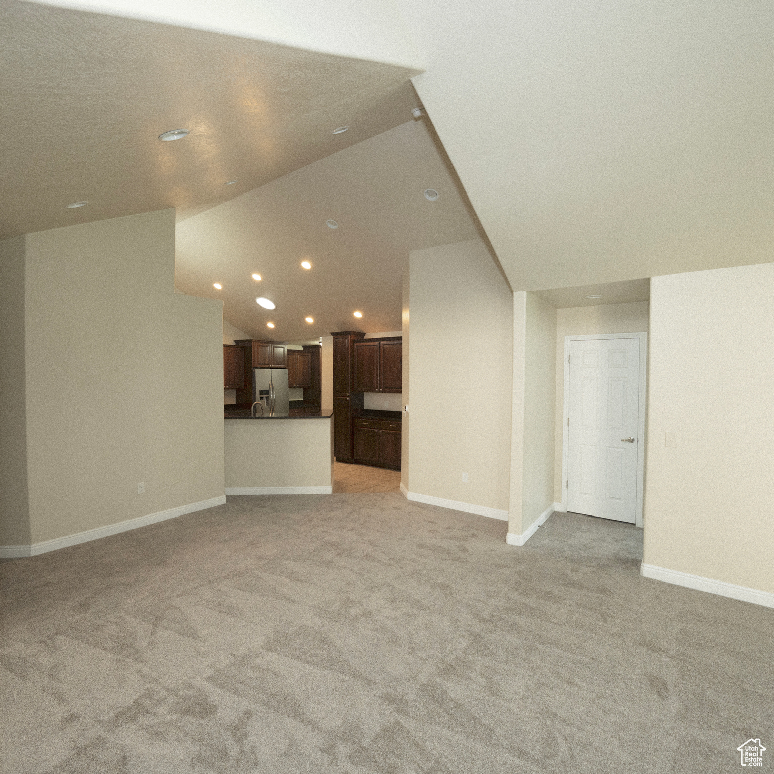 Unfurnished living room featuring light carpet and lofted ceiling