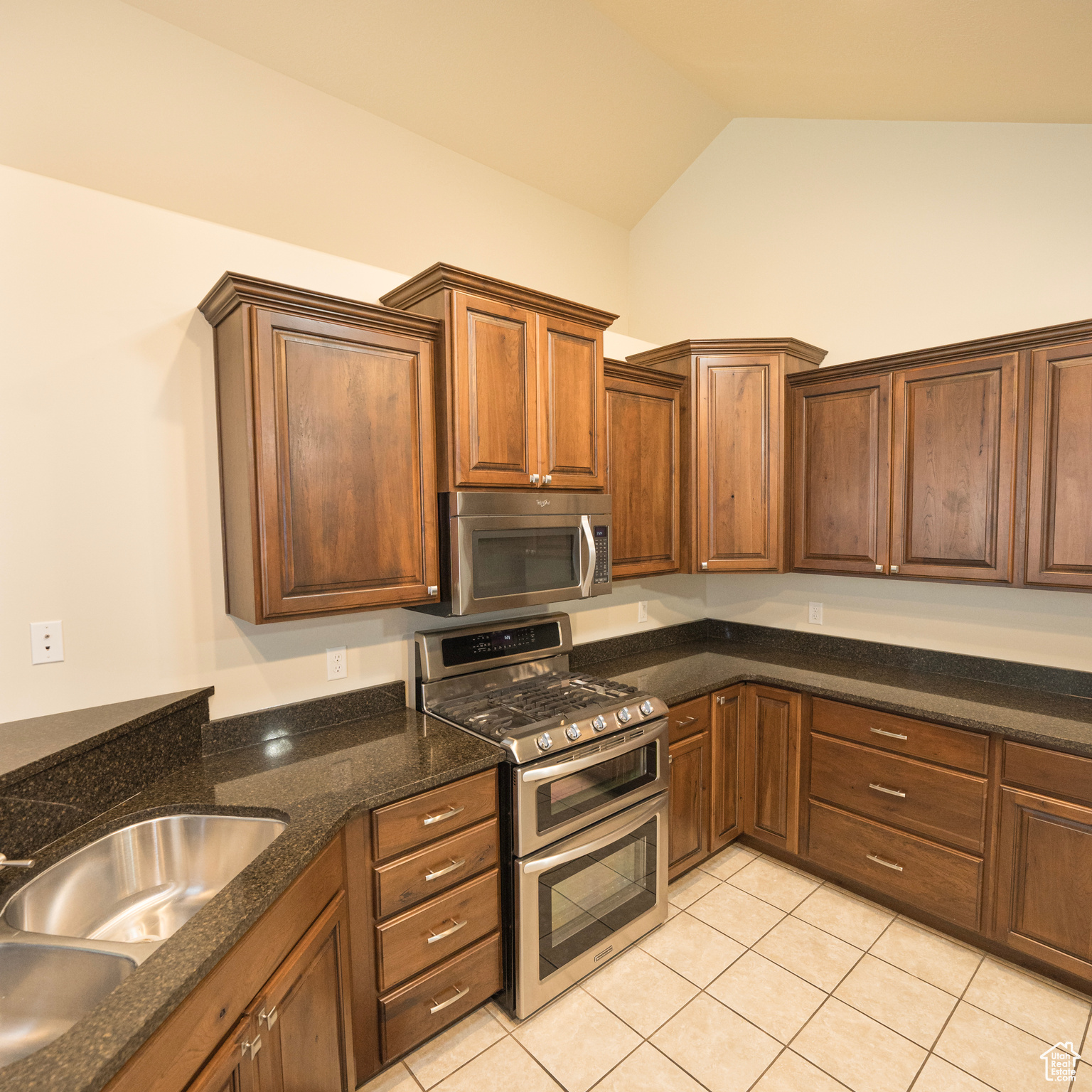 Kitchen featuring light tile patterned floors, lofted ceiling, sink, and appliances with stainless steel finishes