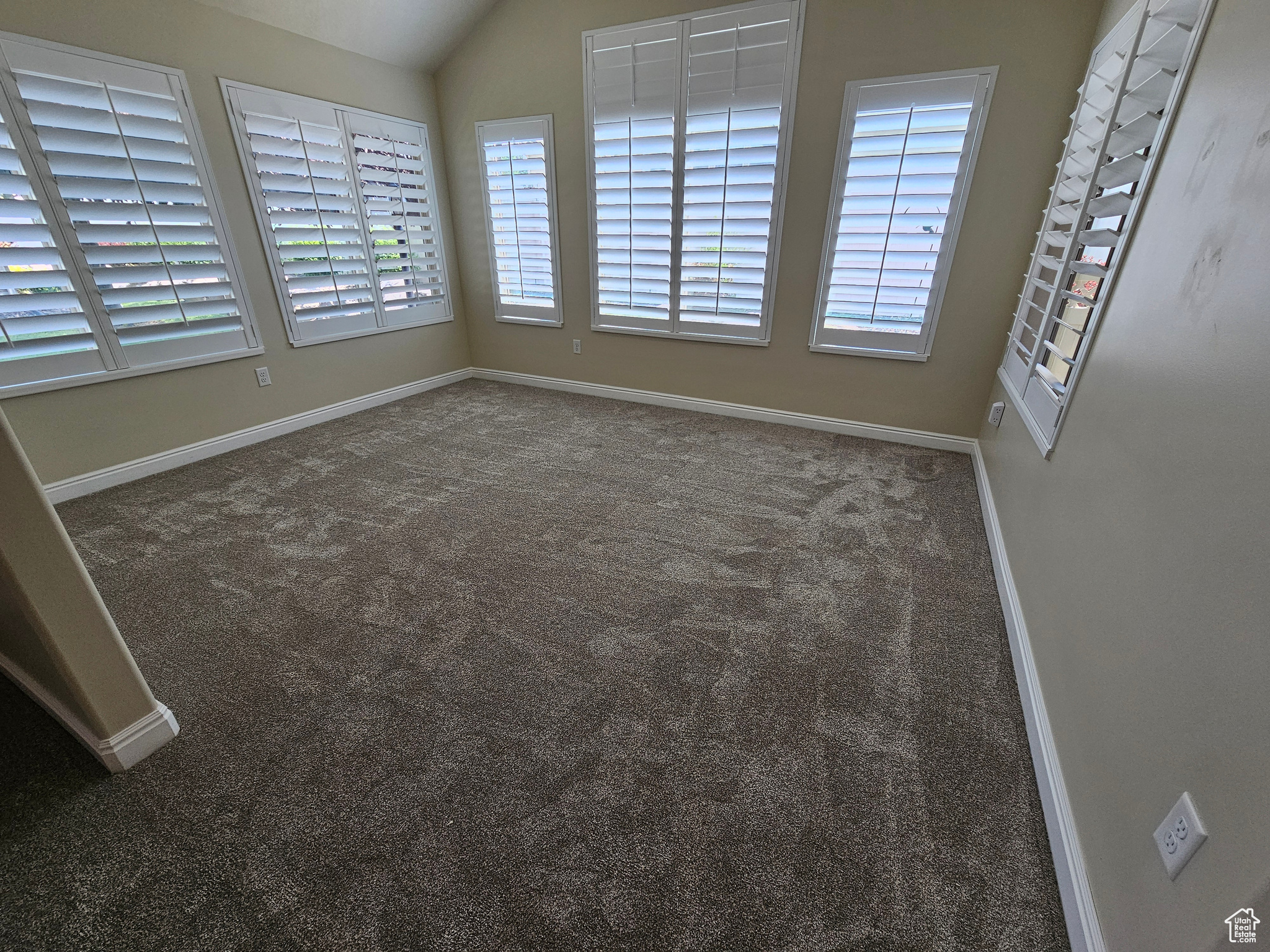 Empty room with vaulted ceiling and dark colored carpet