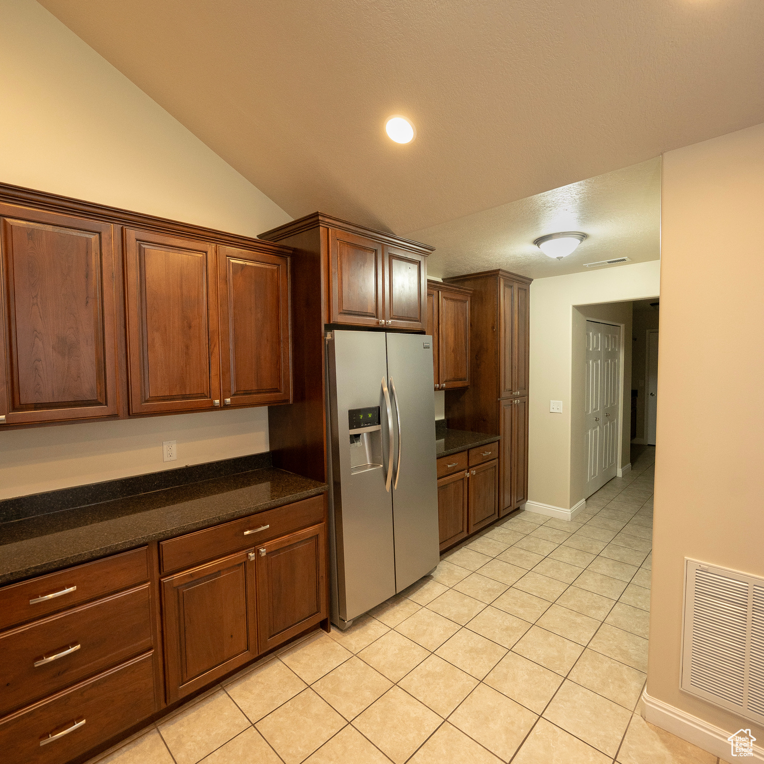 Kitchen featuring stainless steel fridge, dark stone counters, lofted ceiling, and light tile patterned flooring