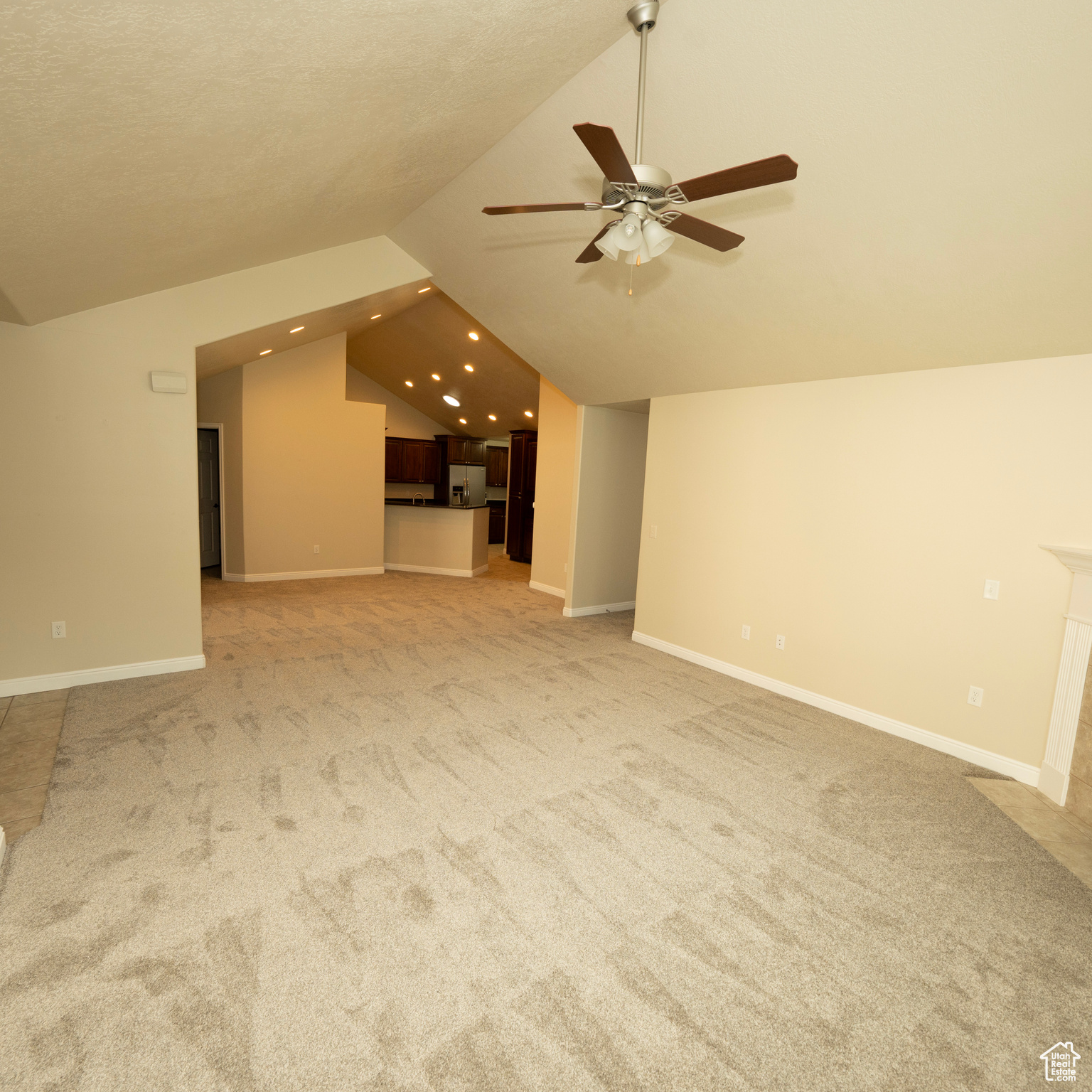 Unfurnished living room featuring carpet floors, vaulted ceiling, ceiling fan, and a tiled fireplace