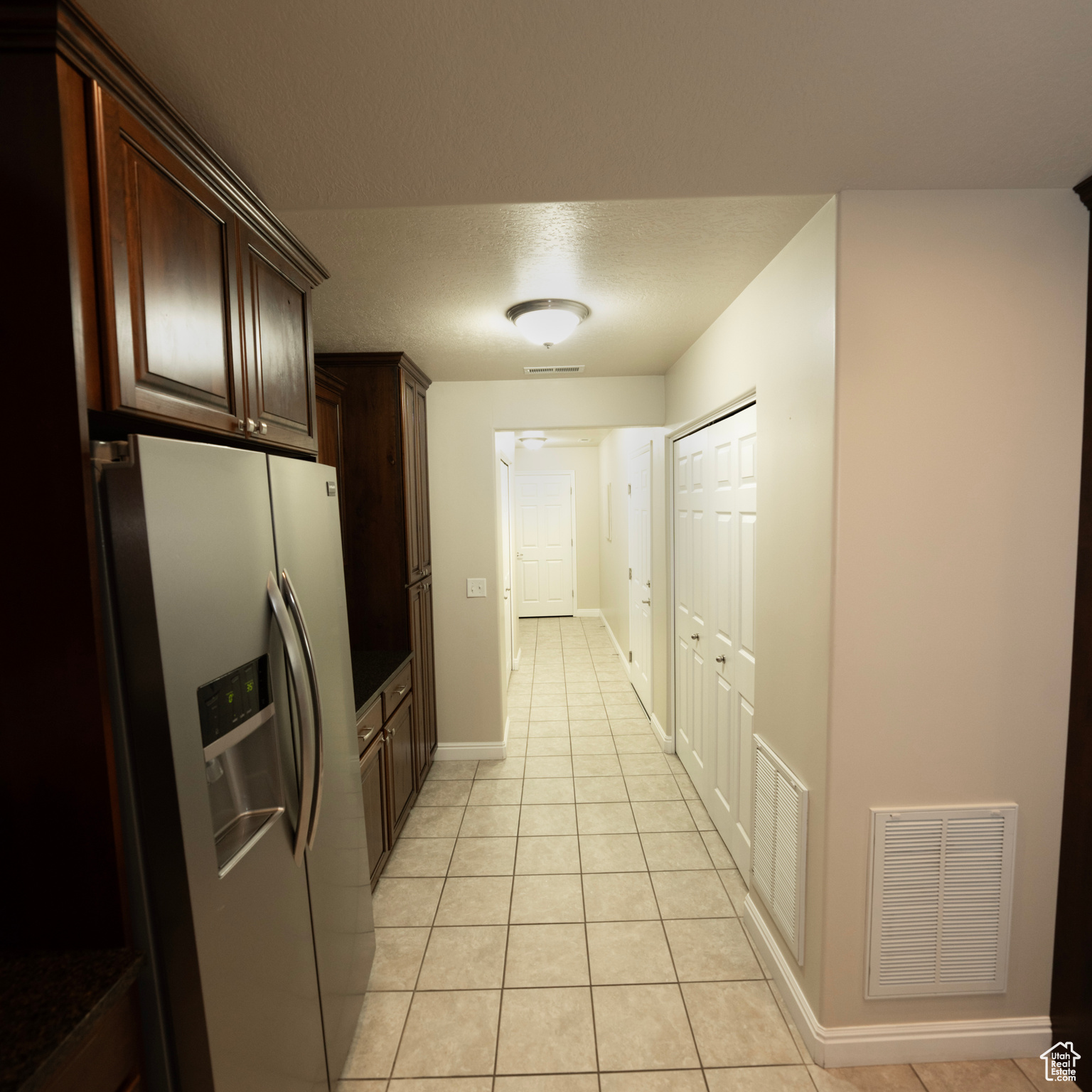 Kitchen featuring dark brown cabinets, stainless steel fridge with ice dispenser, a textured ceiling, and light tile patterned floors