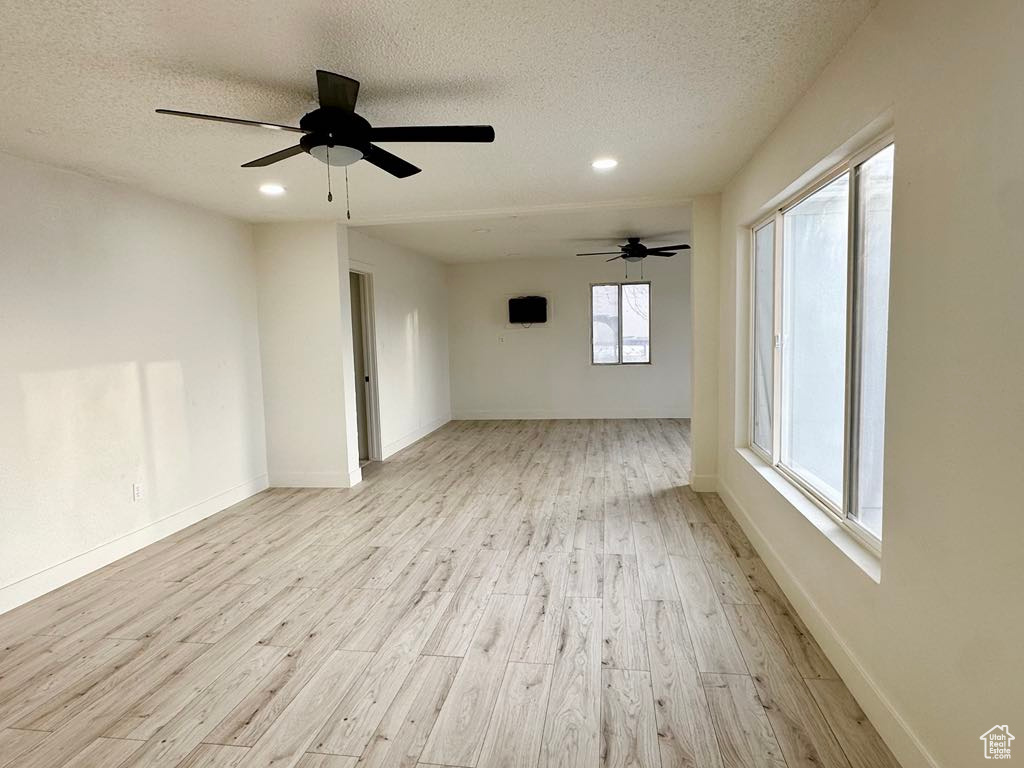 Empty room with a textured ceiling, light hardwood / wood-style floors, and ceiling fan