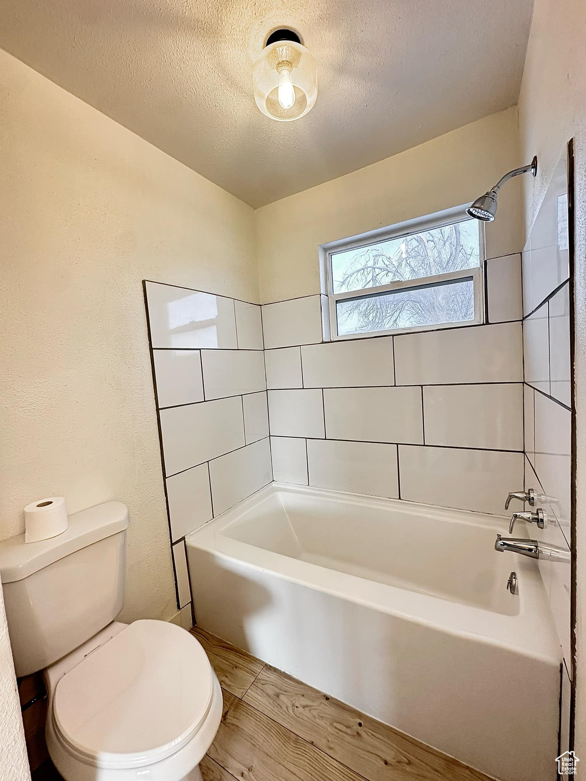 Bathroom featuring a textured ceiling, toilet, and tiled shower / bath