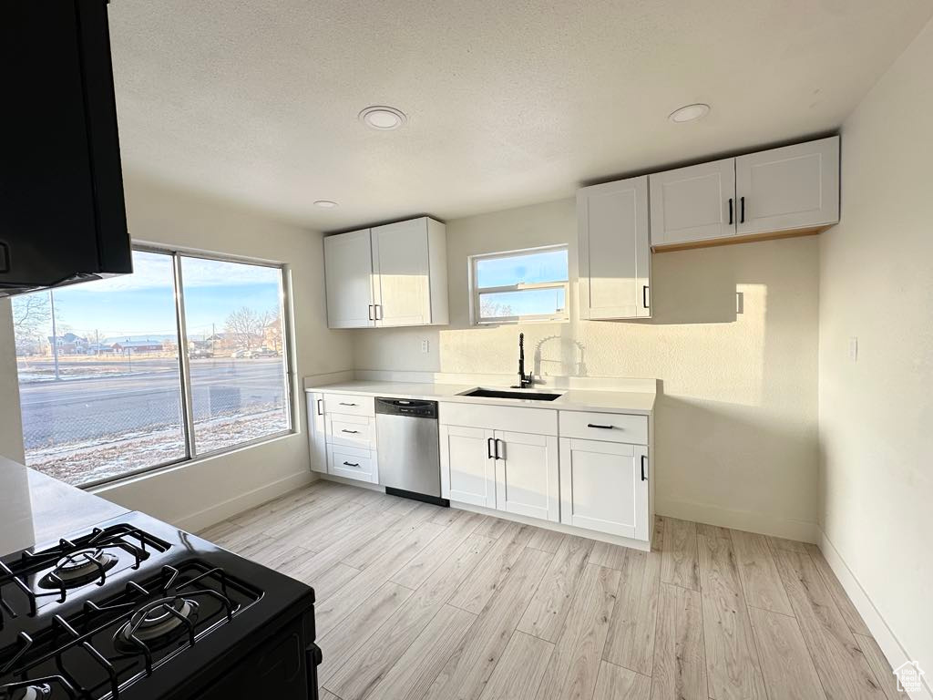 Kitchen featuring light wood-type flooring, white cabinets, sink, black range, and dishwasher