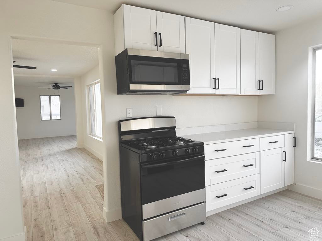 Kitchen featuring stainless steel appliances, white cabinetry, ceiling fan, and light hardwood / wood-style flooring